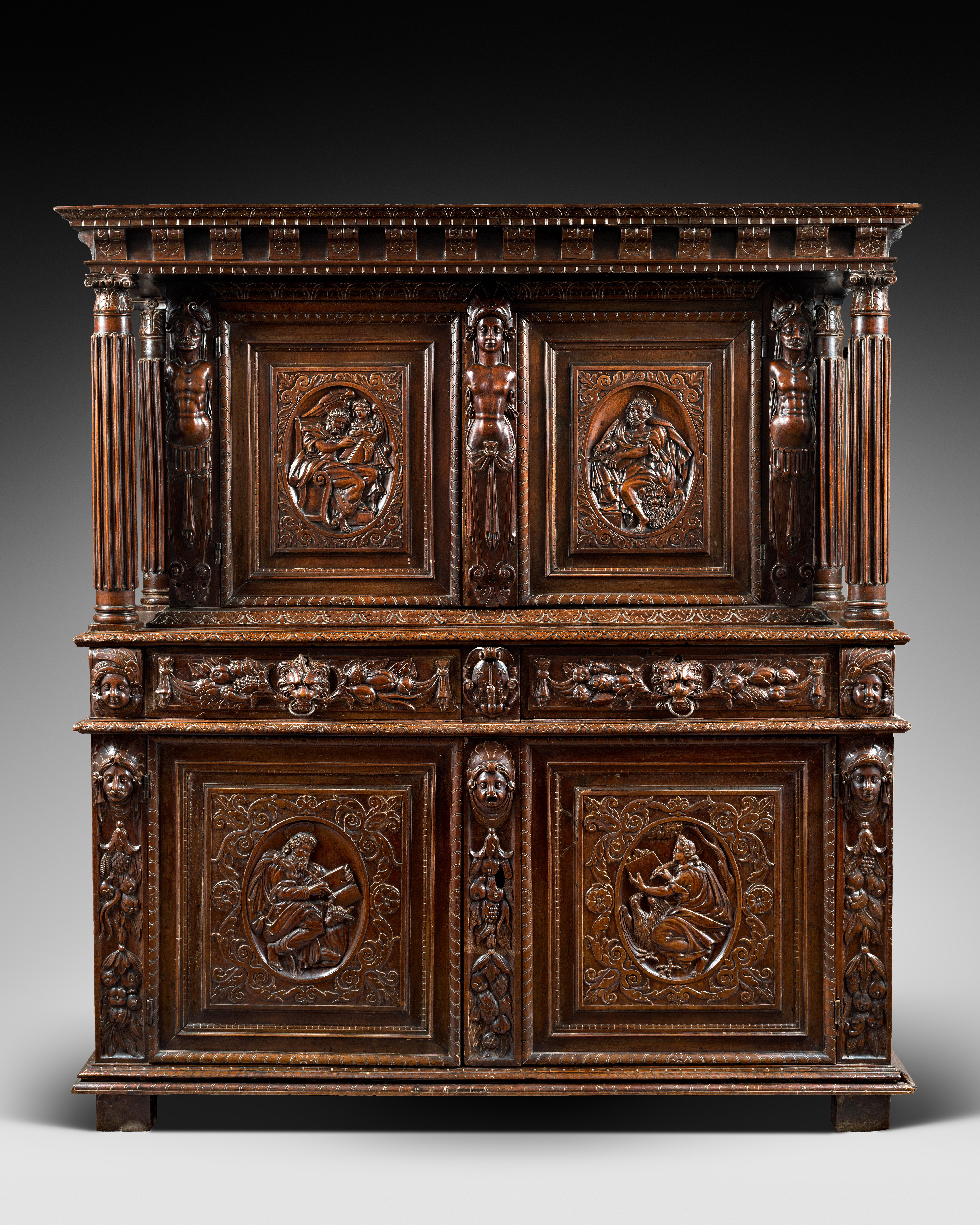 The cabinet’s upper body, slightly recessed is topped by an overlapping entablature and cornice supported both in the front and the rear by four fluted columns. 

The lower body stands on four squared feet and a moulded base. Each door-leaf’s