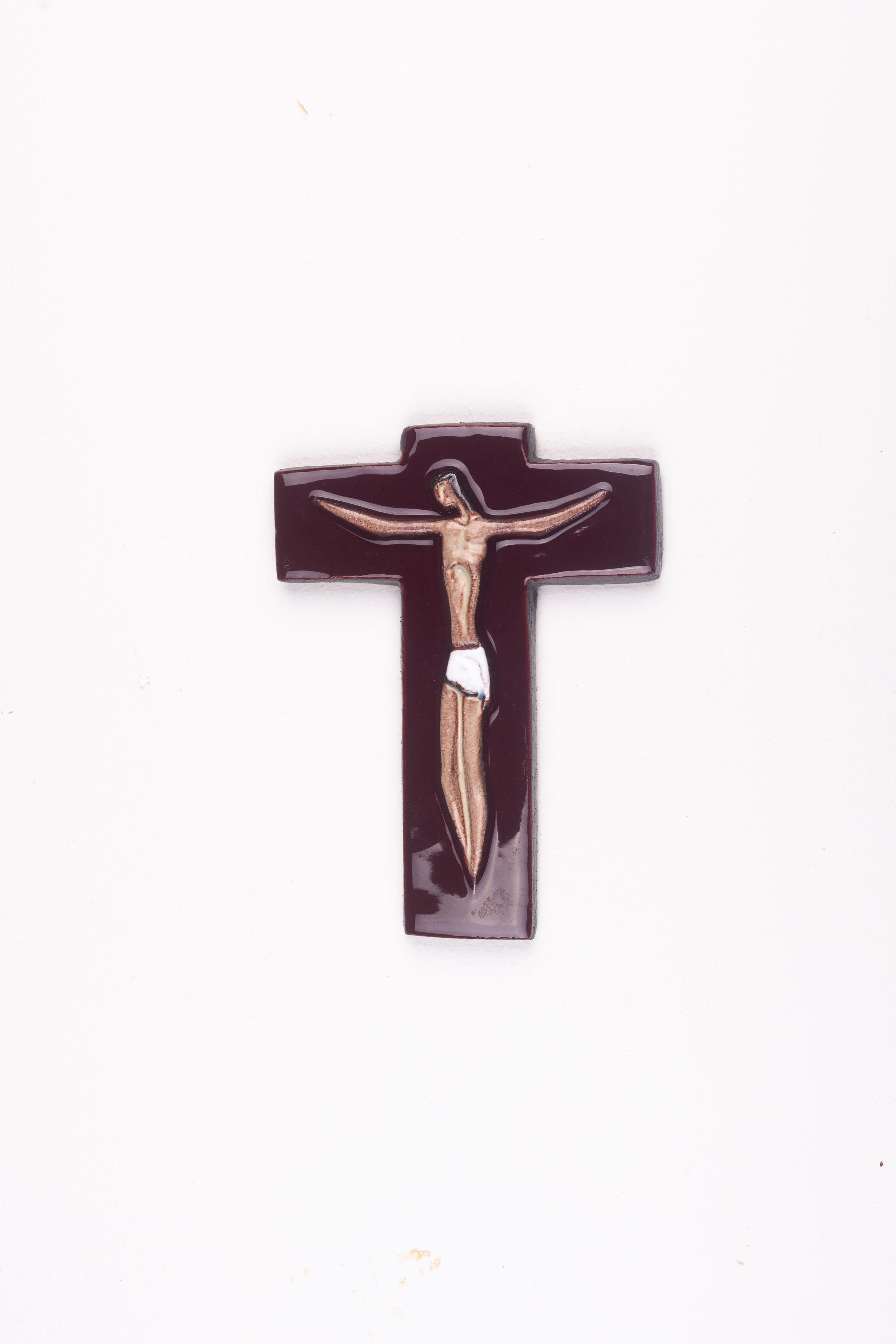 Crafted by Flemish artisans, this midcentury religious cross has a burgundy glossy glaze and sinewy Christ figure at its center. Rendered in fluid lines, the interplay of these with the glossy burgundy glaze, earth tones, and white swath creates a