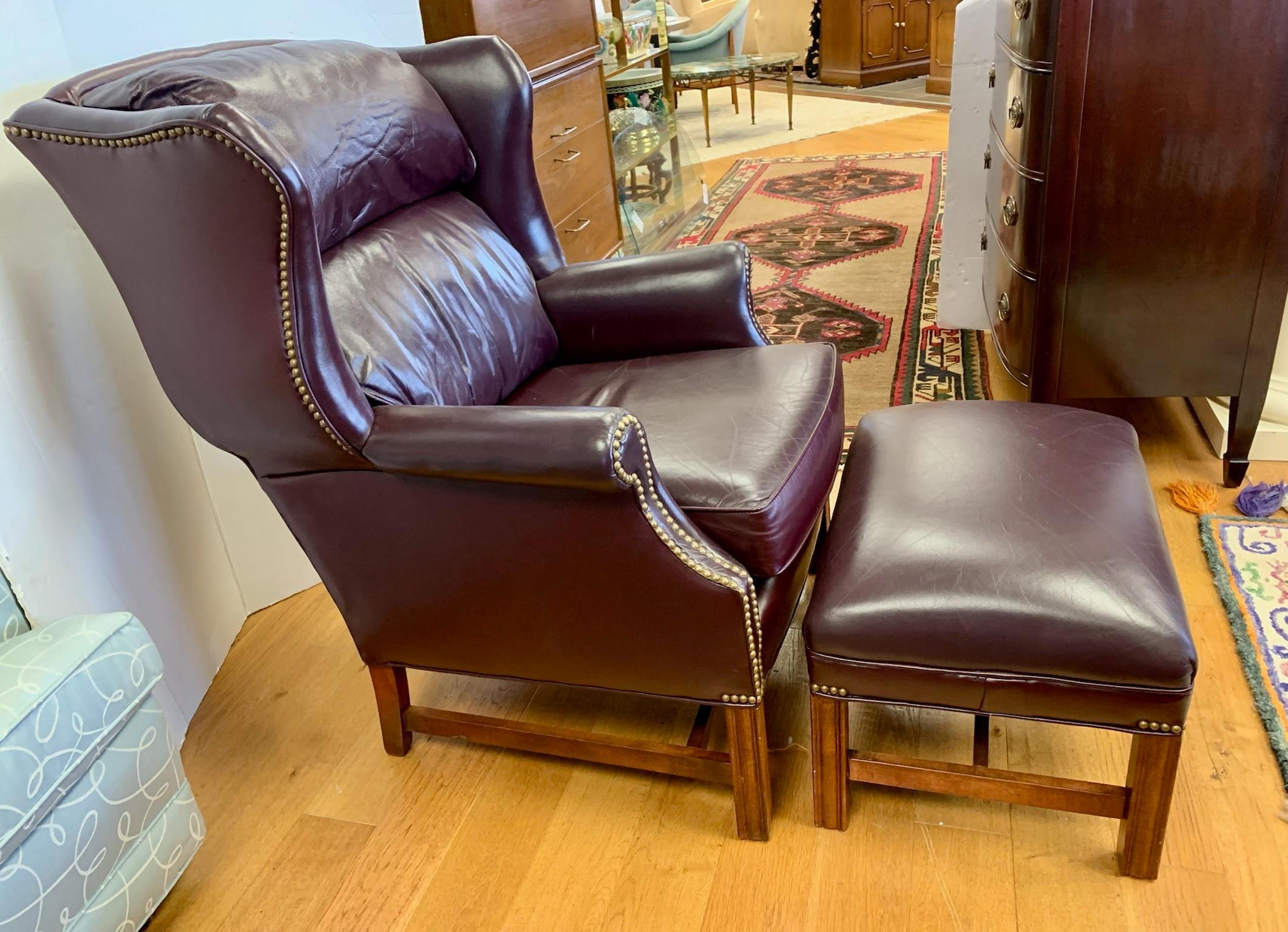 Classic wingback chair and matching ottoman upholstered in a rich burgundy leather and accented with brass nailheads. Chair has attached pillow back for extra comfort. Timeless and well constructed by By Sherrill Furniture.