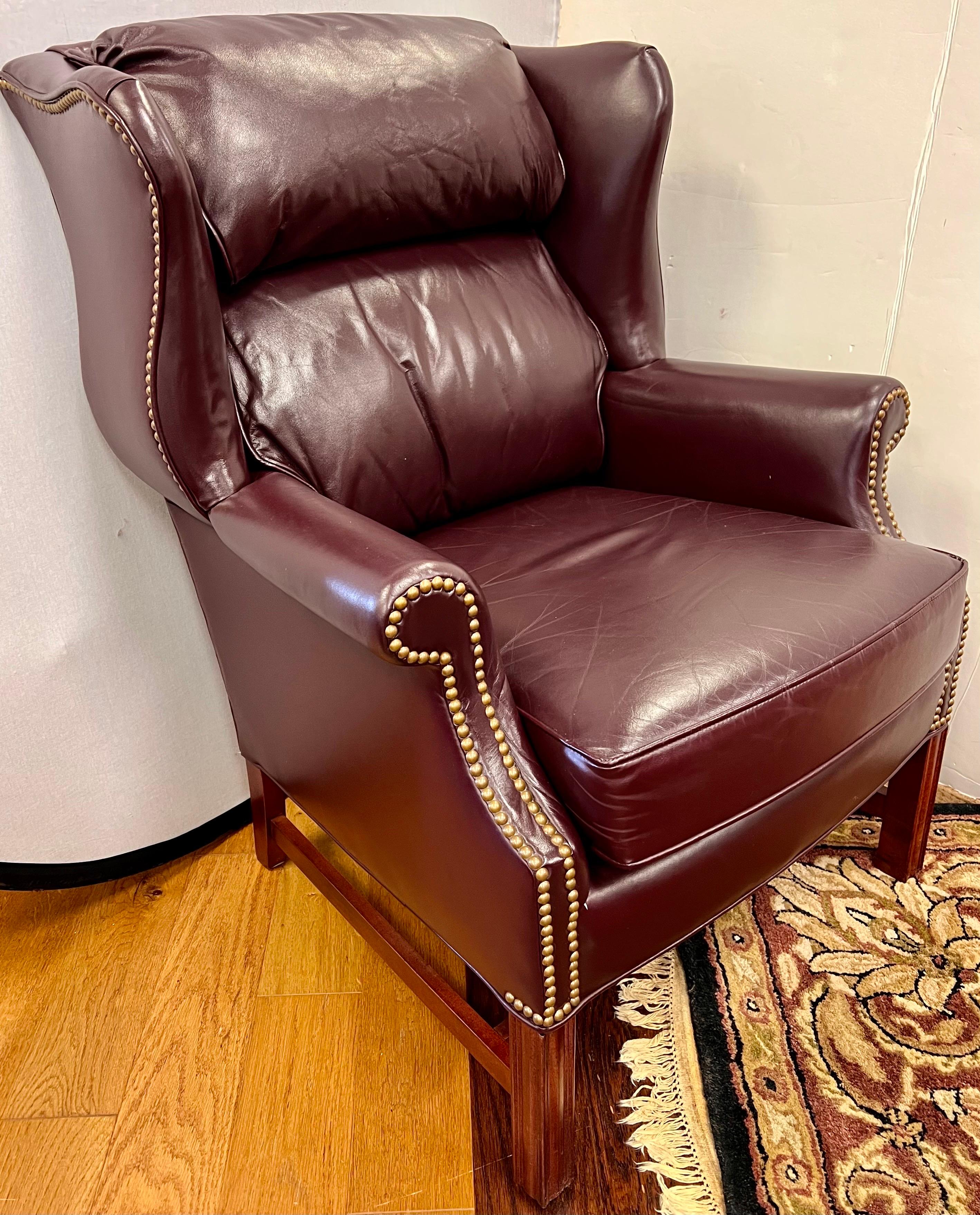 Handsome and luxurious Sam Moore leather wingback chair with rich burgundy color accented with nailhead trim all around and supported by mahogany legs.