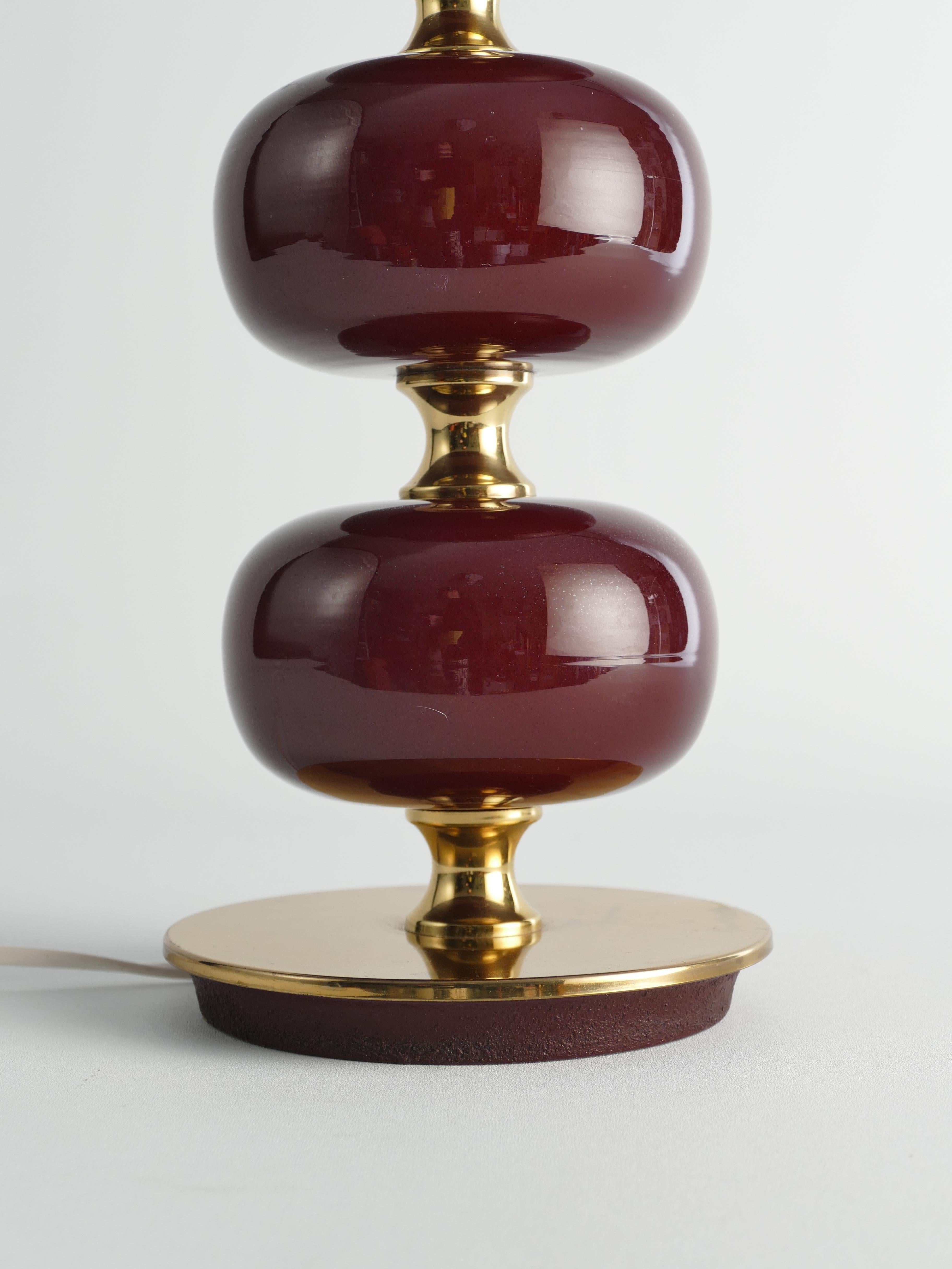 This midcentury table lamp, manufactured by Stilarmatur Tranås in Sweden between the 1960s and 1970s, features three bordeaux red glass spheres with brass feet and details.

Designed by Henrik Blomqvist for Tranås Stilarmatur, this large-sized model
