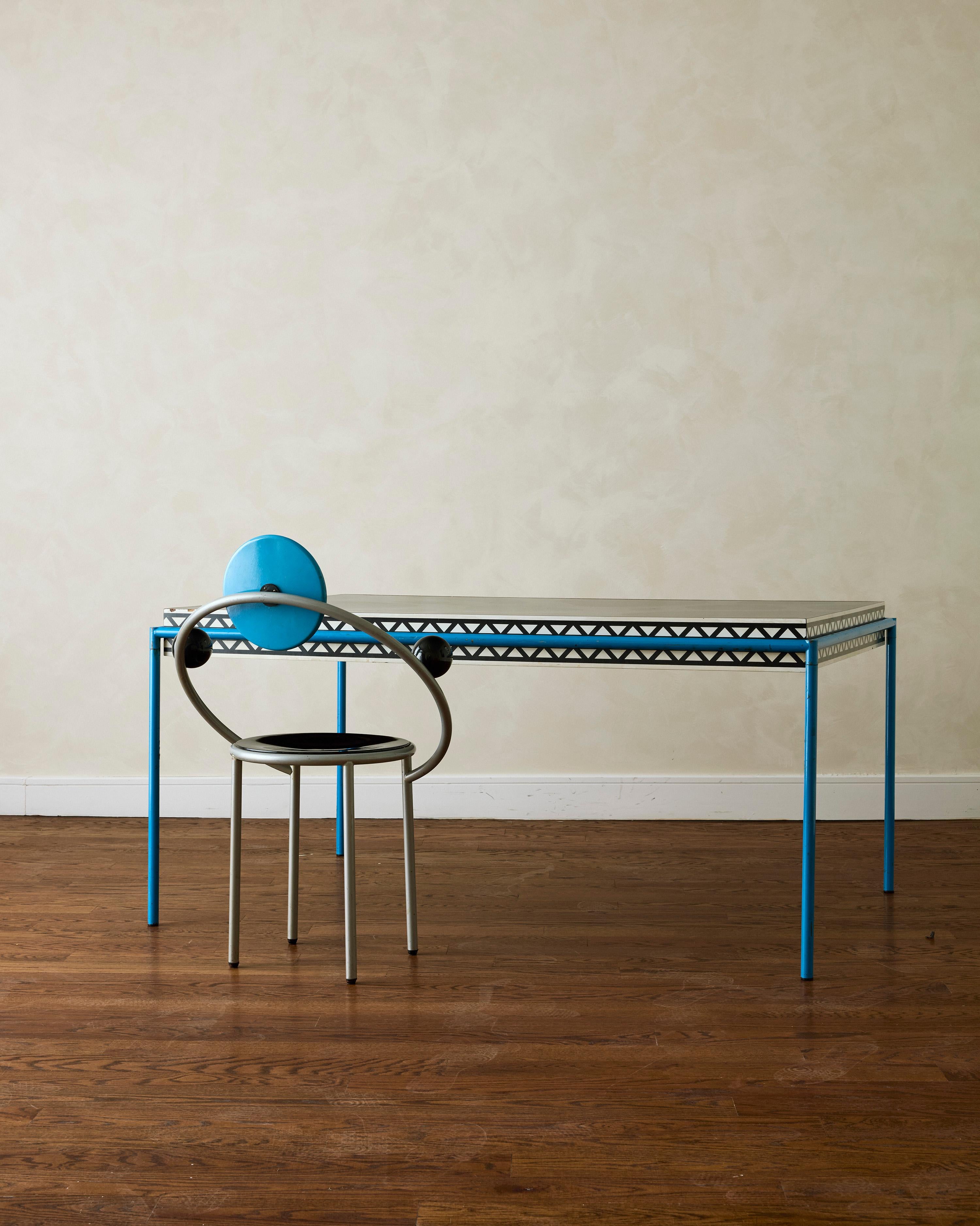 Table de salle à manger et chaise First de Michele De Lucchi. La table est constituée d'un tube d'acier laqué et d'un plateau stratifié. La chaise présente un dossier circulaire laqué bleu, une assise laquée noire et des objets sphériques laqués