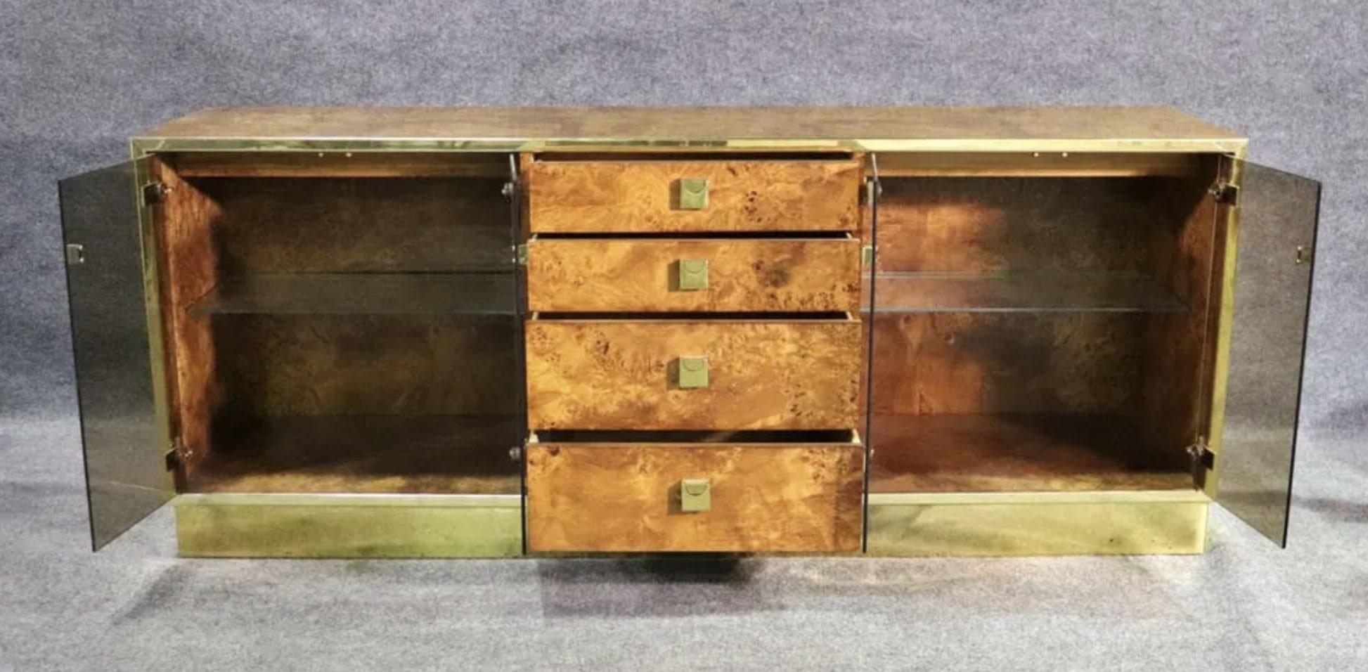 Beautiful mid-century modern credenza by Founders. Designed with a  combination of bright burl wood grain and polished brass. Two cabinets on either side with smoked glass doors each have interior lights to properly display your decorative