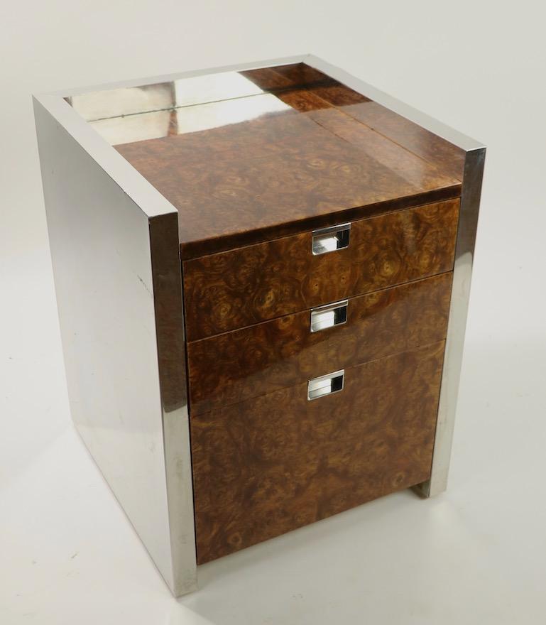 Chic burl and chrome stand having bright chrome sides with high gloss burl drawer fronts and top surface. The cabinet has three drawers, and is well constructed however there are some condition issues as follows. The chrome trim on one top edge has