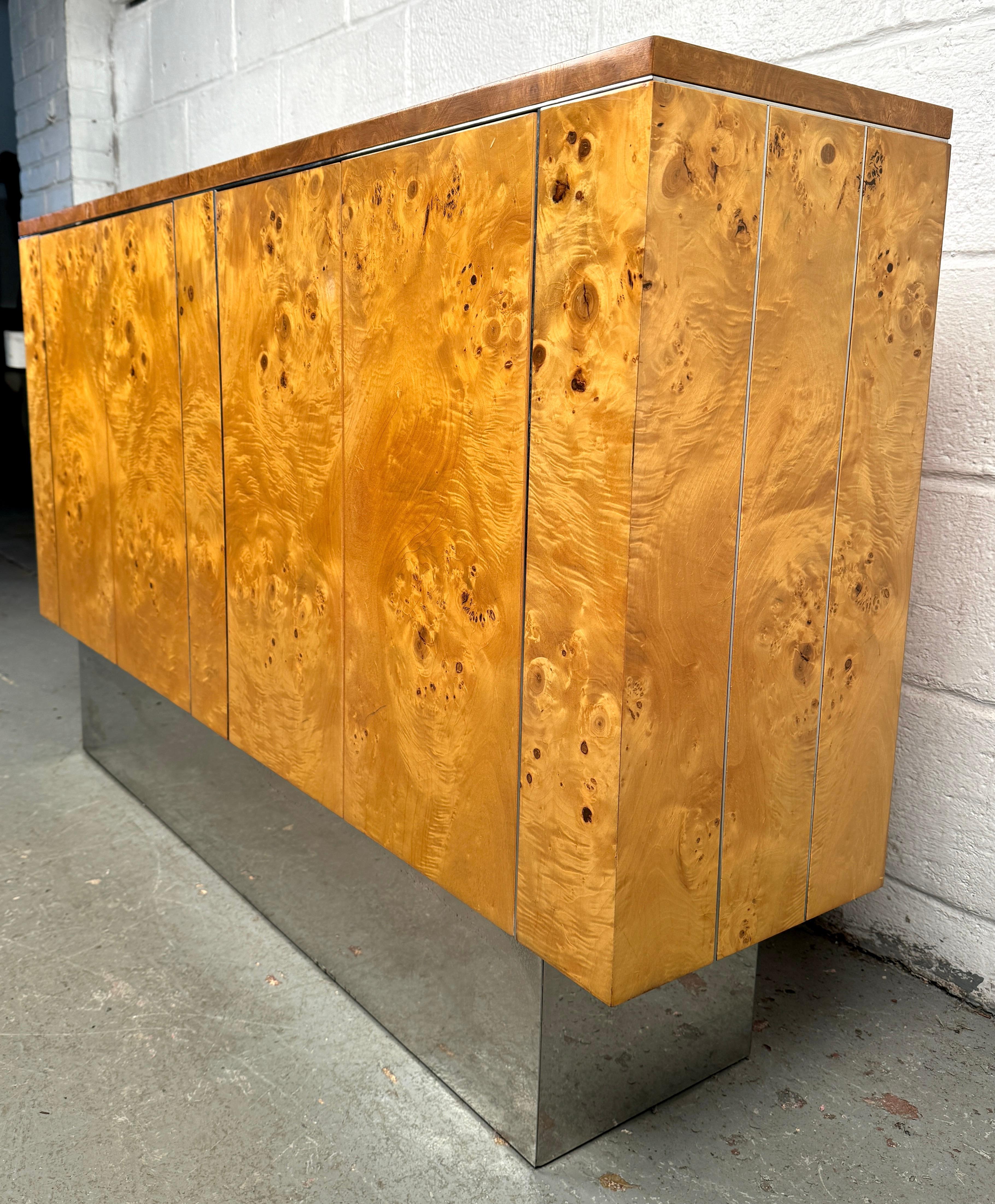 A striking burl console table in the style of Thomasville, featuring a richly figured veneer top with sharp, clean edges that lend a modern edge to its classic form. The sleek metal base adds contrast and sophistication, creating a bold blend of