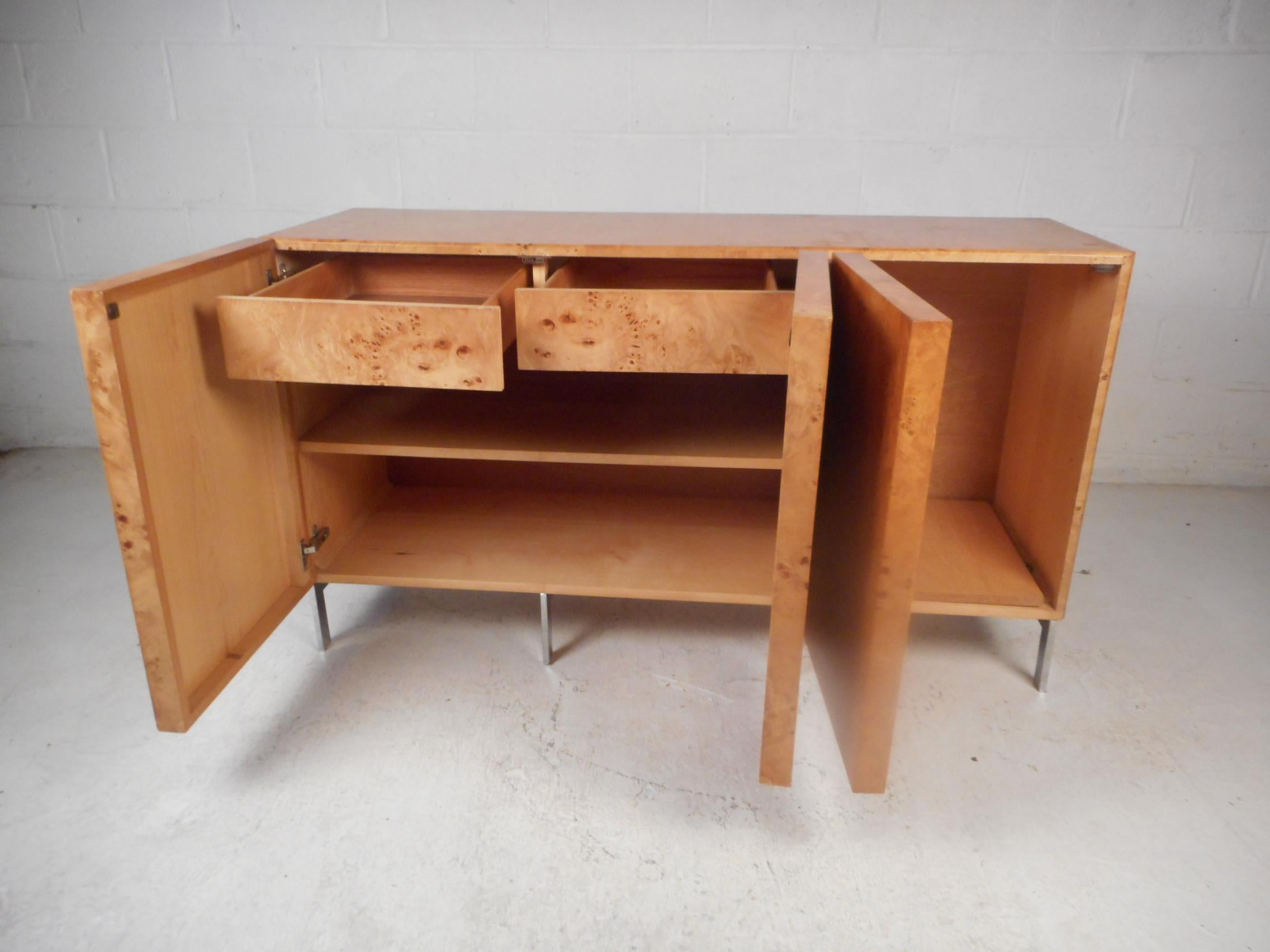 Stunning midcentury credenza in the style of Milo Baughman. Burl maple adorns the entirety of the piece's exterior. Supported by stylish chrome base. Two cabinets with drawers and shelving offer ample storage space. This piece is sure to make a