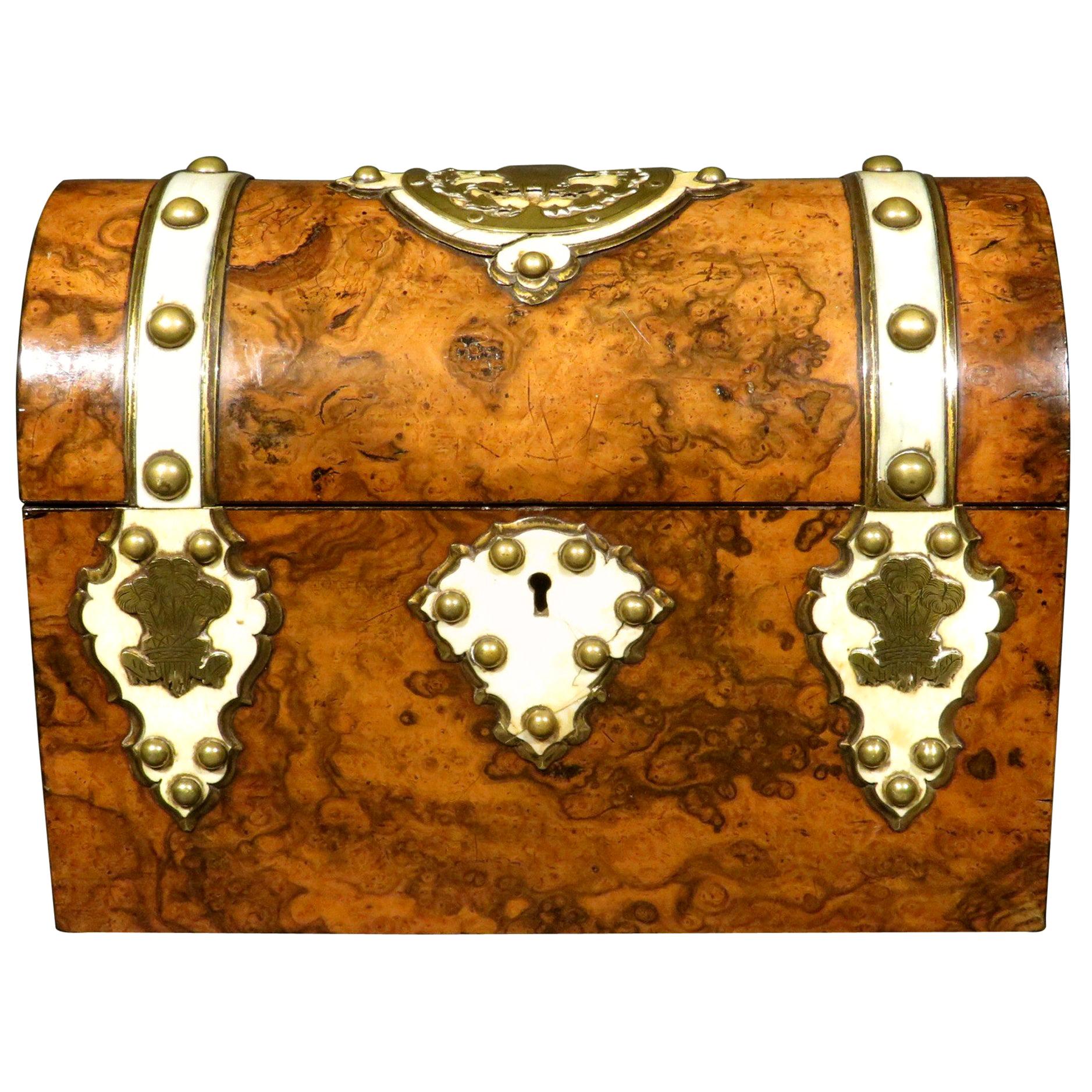 The highly figured burl walnut exterior banded with bone strapping and applied brass elements, the domed lid centred by a pierced brass cartouche engraved with the Prince of Wales Feathers together with the motto ‘Ich Dien’ (I Serve), repeated again