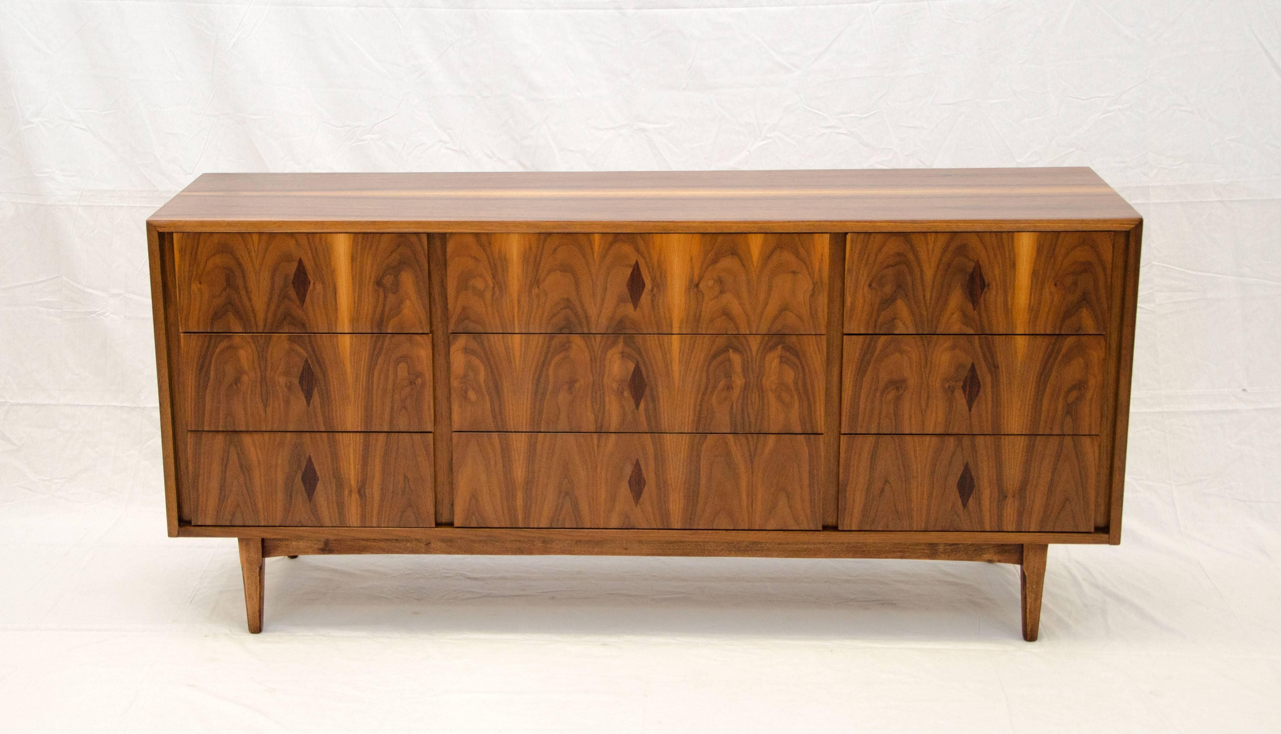 Very nice midcentury nine-drawer walnut dresser or chest with bookmatched grain patterns. There are diamond shaped rosewood inlays positioned in the center or each drawer. The dovetailed drawers have finger insets at the sides and open and close