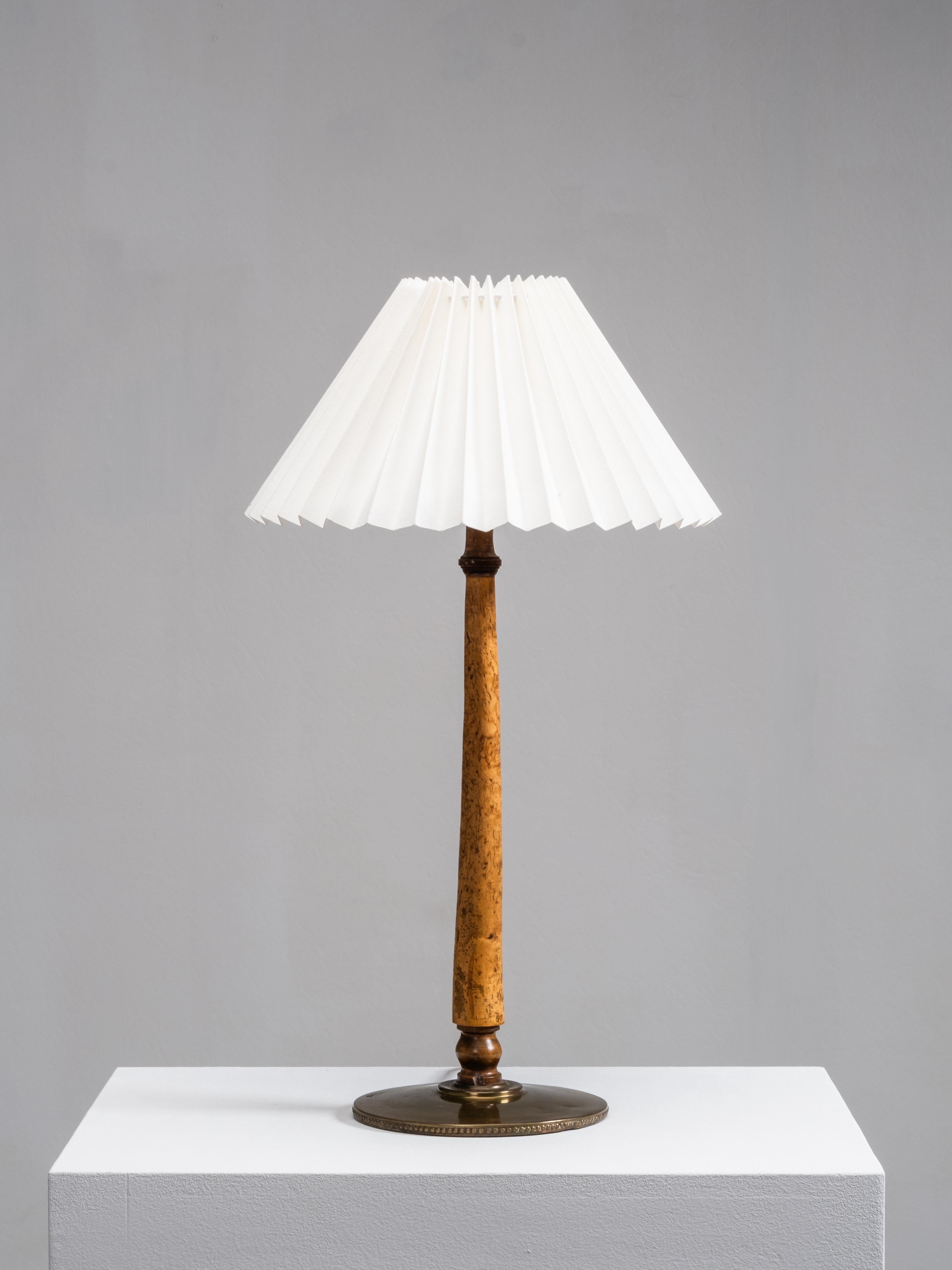 Lampe de table finlandaise des années 1940, finement travaillée, combinant une tige en bois de ronce tourné et une base en laiton massif. Le motif riche et organique du bois contraste avec le laiton lisse et patiné, tandis que l'abat-jour en tissu