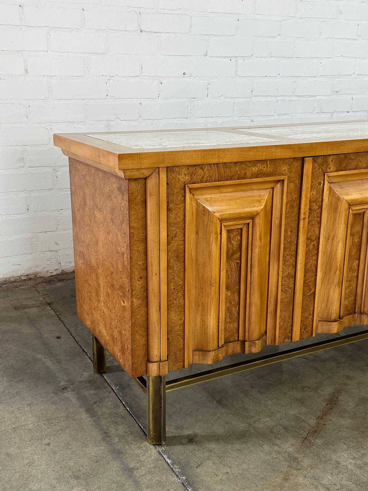 W76 D20.25 H31

1960’s Burl wood, brass & Travertine credenza by J.L. Metz. Item has not been refinished but is in great vintage condition. Credenza features a brass stretcher, inset travertine tops and Burl wood through out. Credenza has sculpted