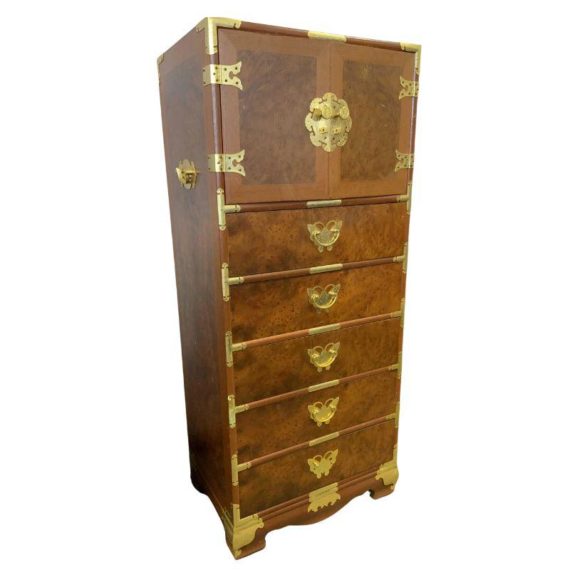 A vintage burl wood campaign style tall chest with brass butterfly design details.  The chest of drawers has two doors at top that open to small drawers inside.  Below the doors are five drawers, each with a butterfly design to the brass hardware. 
