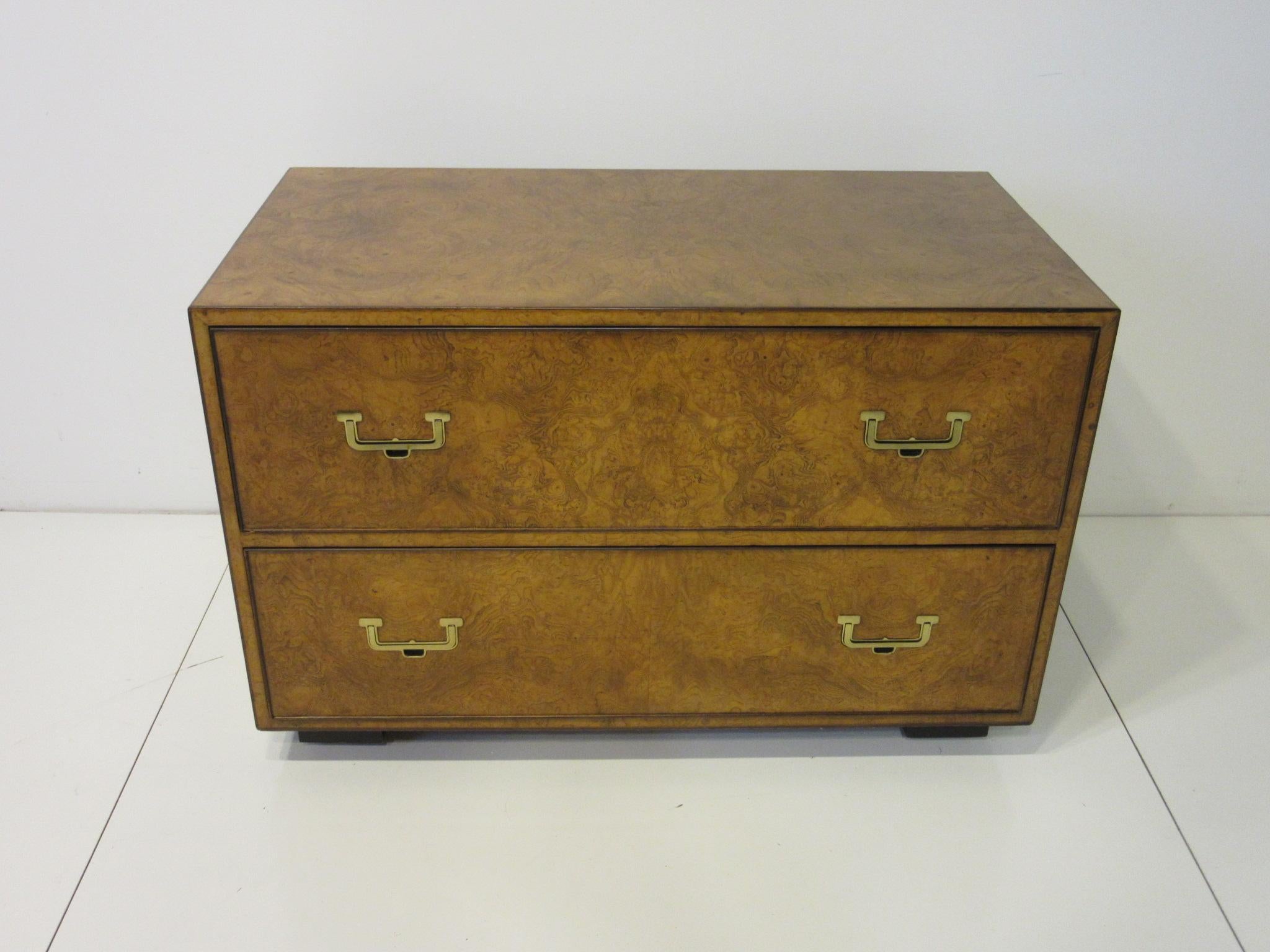 A beautifully burled book matched finished two-drawer low chest having inset brass pull handles and black legs with roller ball wheels to the bottom. Retains the manufactures label from the John Widdicomb furniture company Grand Rapids Michigan.
