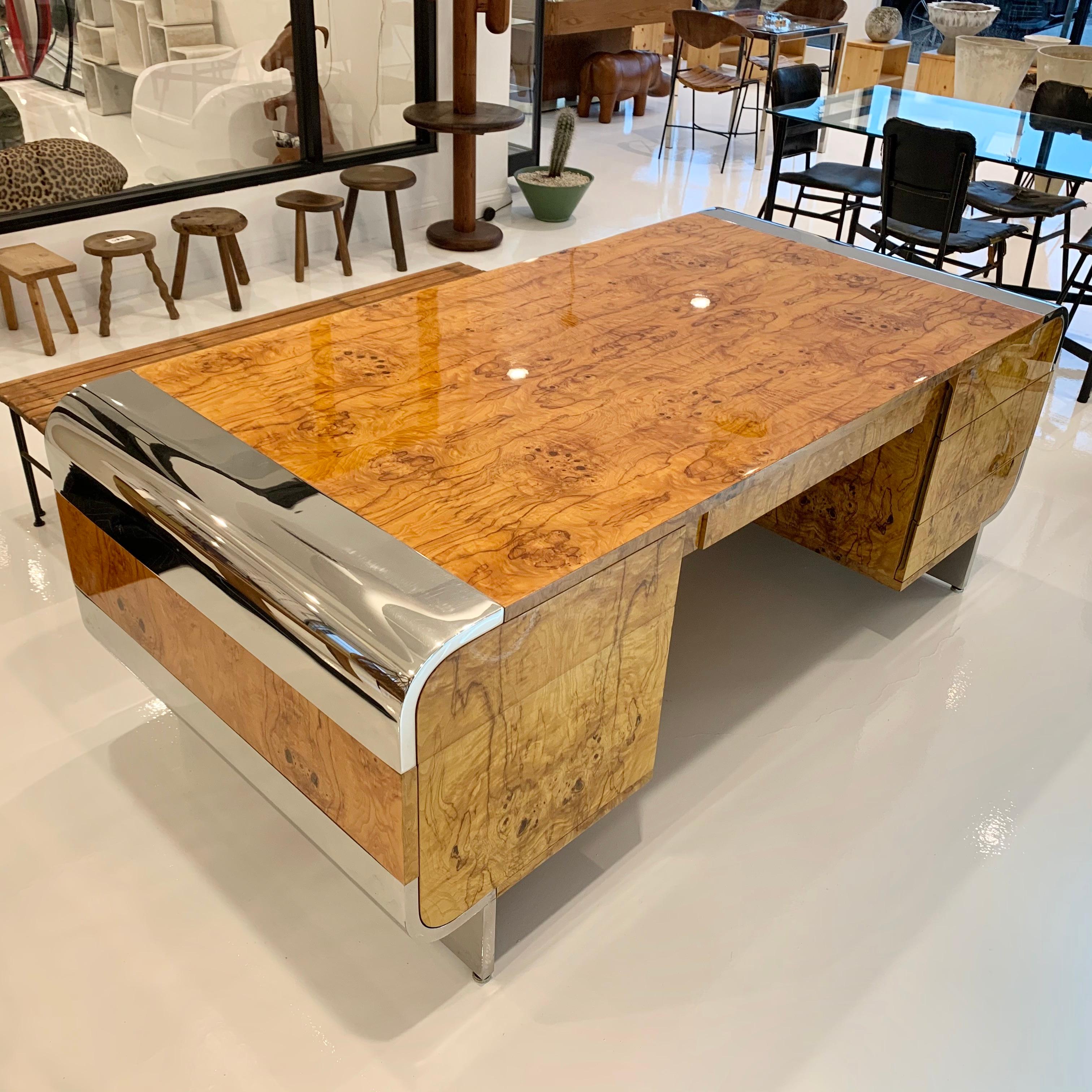 Stunning burl wood and stainless steel desk by Pace, designed by Irving Rosen. Waterfall edges with polished stainless steel. Wood is a polished Burl. 3 drawers flank the left side and two drawers flank the right side, including a large file drawer.