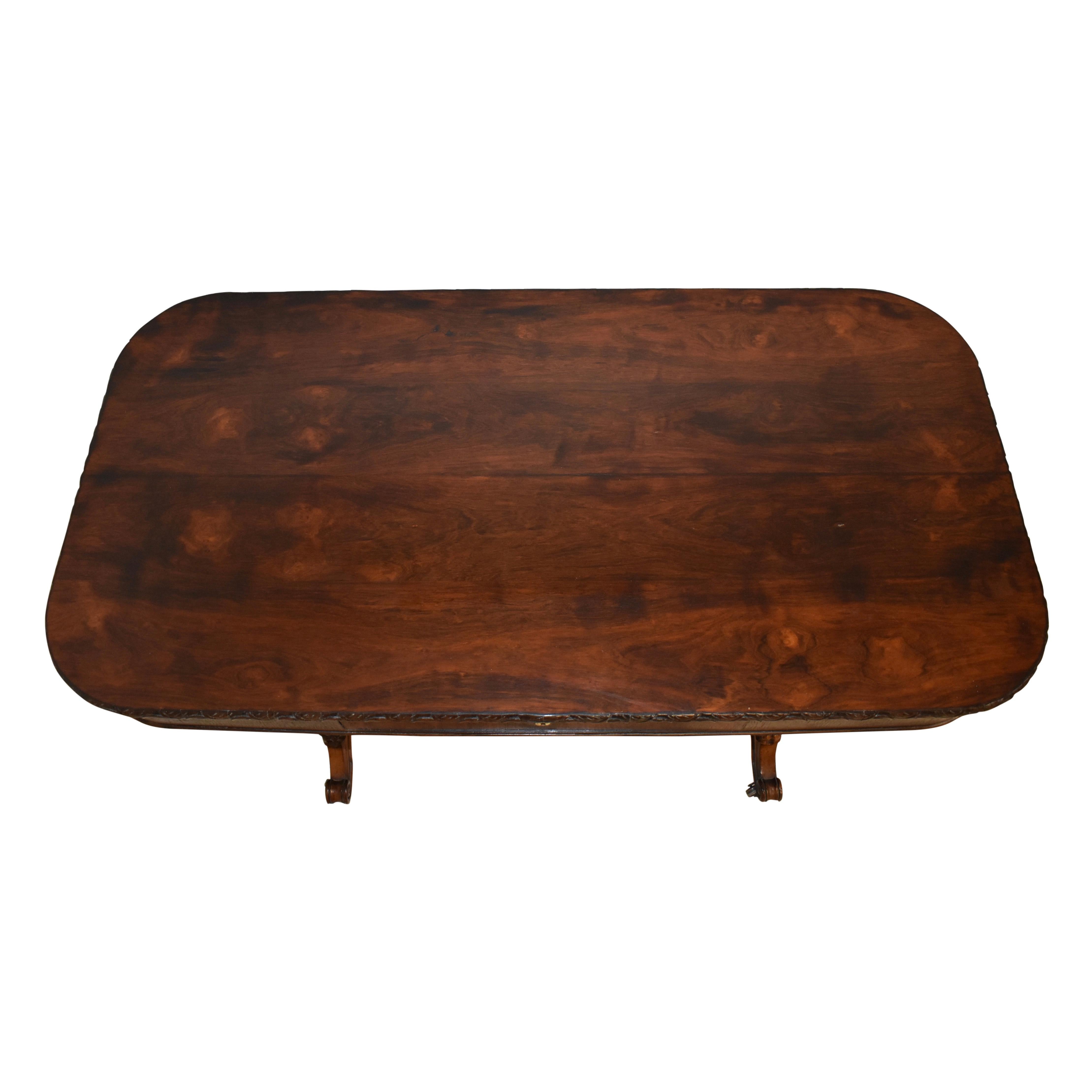 Featuring a beautiful burled, veneer top over oak with rounded corners and a carved edge, this table is raised on two mahogany turned legs, which terminate in scrolled feet with carved flowers at their centers. A turned stretcher unites the legs,