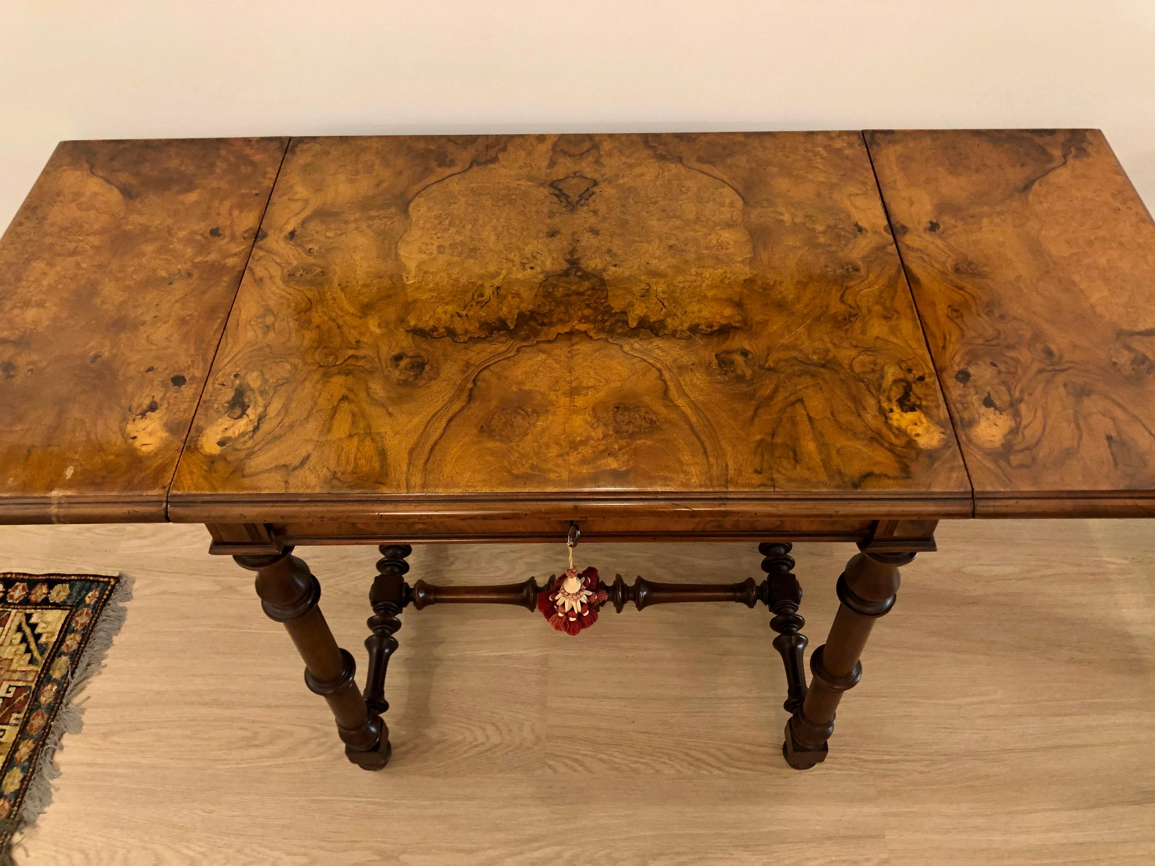 A small, burled walnut table with two drop leaves and a single pull drawer. The table is raised on turned legs with an H form stretcher.  This piece has a gorgeous patina and bookmarked veneer. The lines are simple but the craftsmanship is