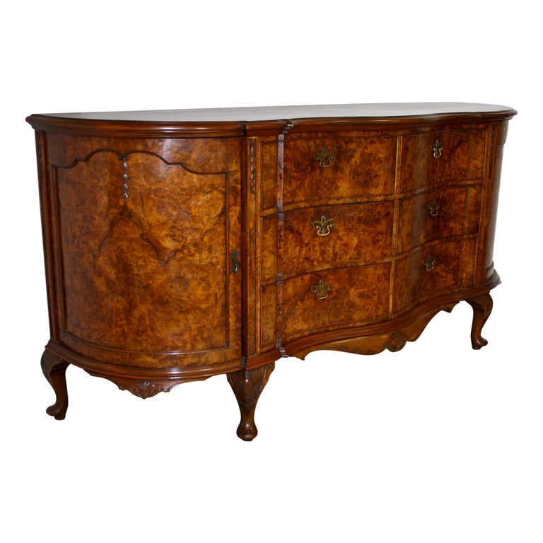 Made of beautiful walnut and burled walnut veneers with a well figured, unique grain, this sideboard features a serpentine front; two center columns of three drawers, flanked by curved doors with arched, recessed panels; and carved, scalloped