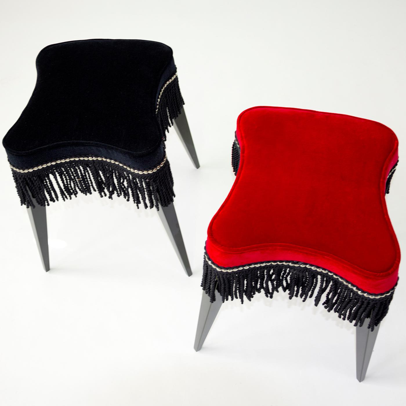 Lovely and eclectic stool with black lacquered wooden legs. The seat is upholstered with red velvet embellished with visible studs and black fringes. The ironic and original design makes this piece of furniture so versatile that it can be combined