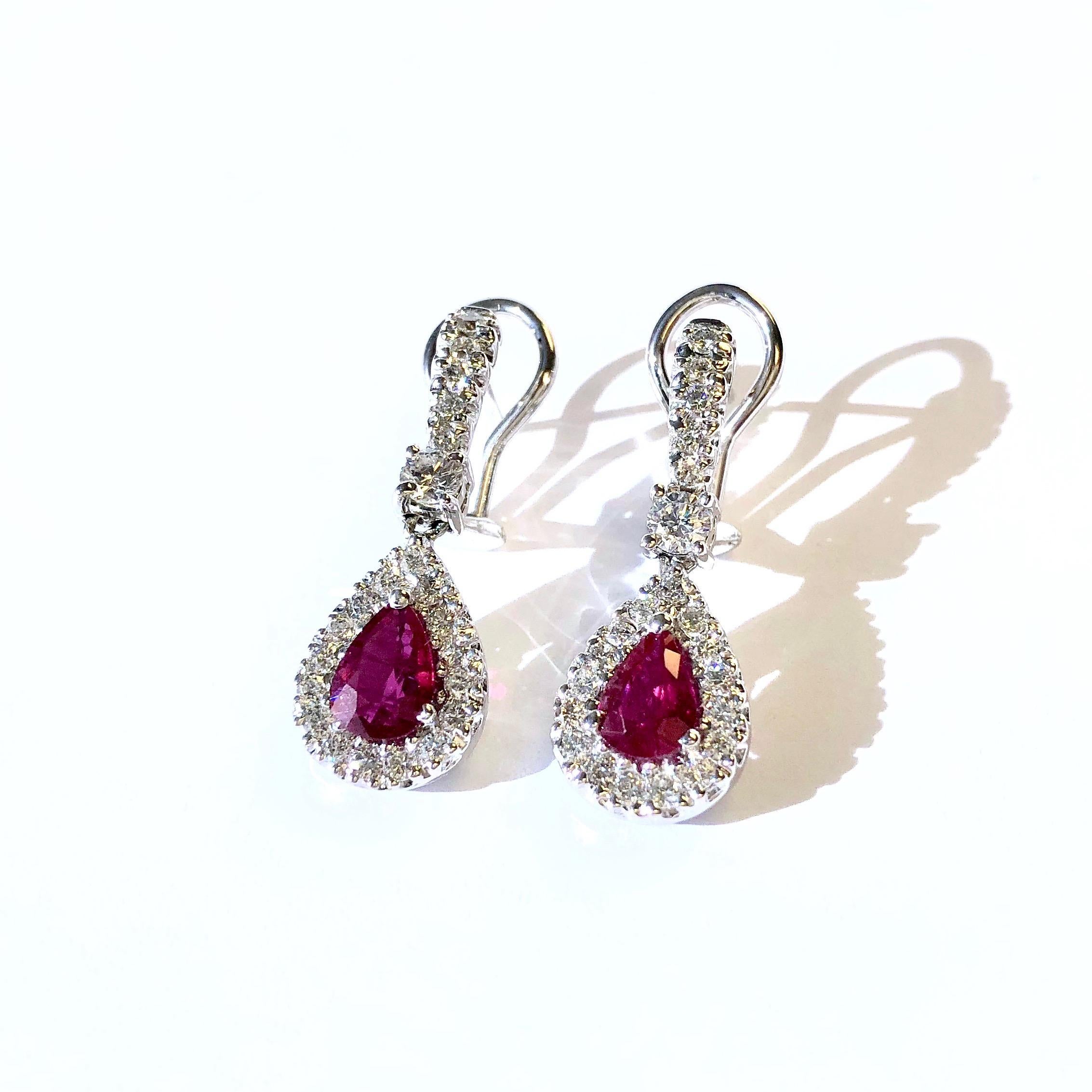 Crafted in 18K white gold, each earring features pear shape pendant set with a one carat ruby solitaire in a bezel of diamonds, supported by a diamond set ribbon. Post and omega backings for added security. 
44 round brilliant cit diamonds,