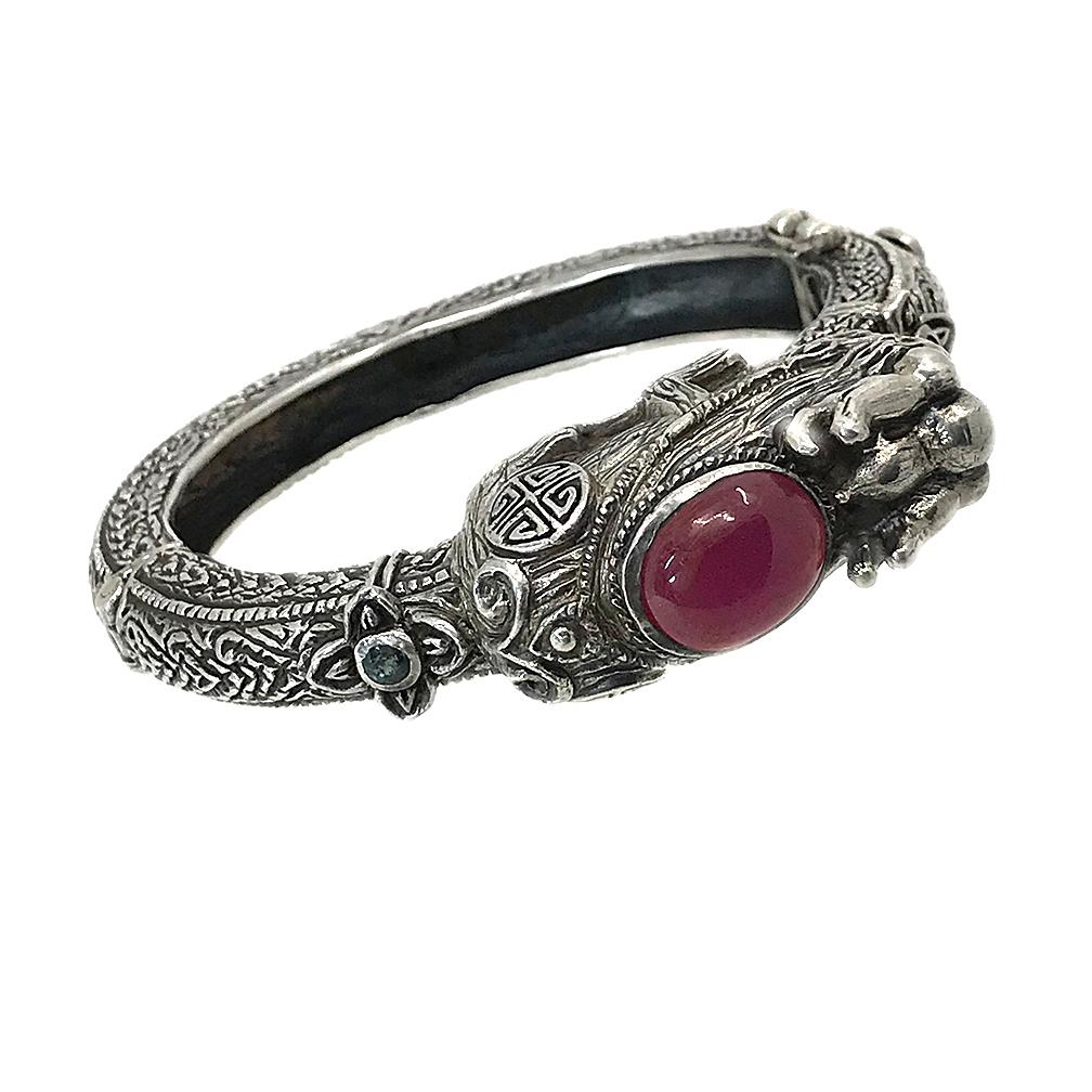 This is a Burma Ruby and sterling silver dragon cuff. A large Burma Ruby cabochon bezel sits on top of a dragon head with a detailed textured body. The 6.25 inch inner circumference cuff is marked 925 inside of the body and comes with an extra
