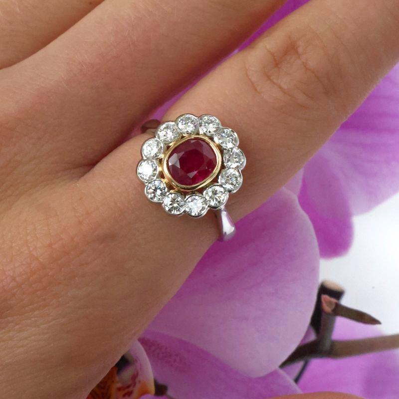 A Burma ruby, diamond and platinum cluster ring, set with a 0.97 carat, oval, faceted Burma ruby, in a gold rub over setting, with a surrounding cluster of twelve, round brilliant-cut diamonds, in rub over settings, onto a tapered shank, with split