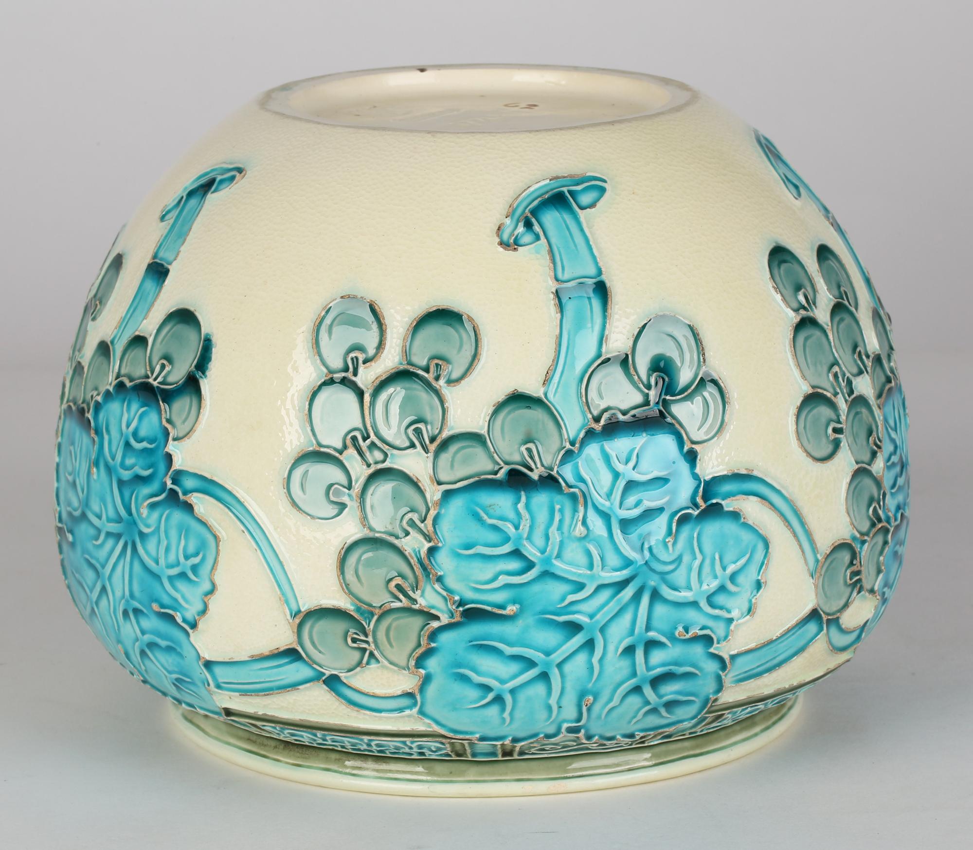 A fine Burmantofts Faience Art Nouveau art pottery bowl decorated with fruiting vines and dating from around 1895. The bowl stands on a narrow round foot with a slightly recessed base with a wide rounded body with a narrower fold over rim. The body