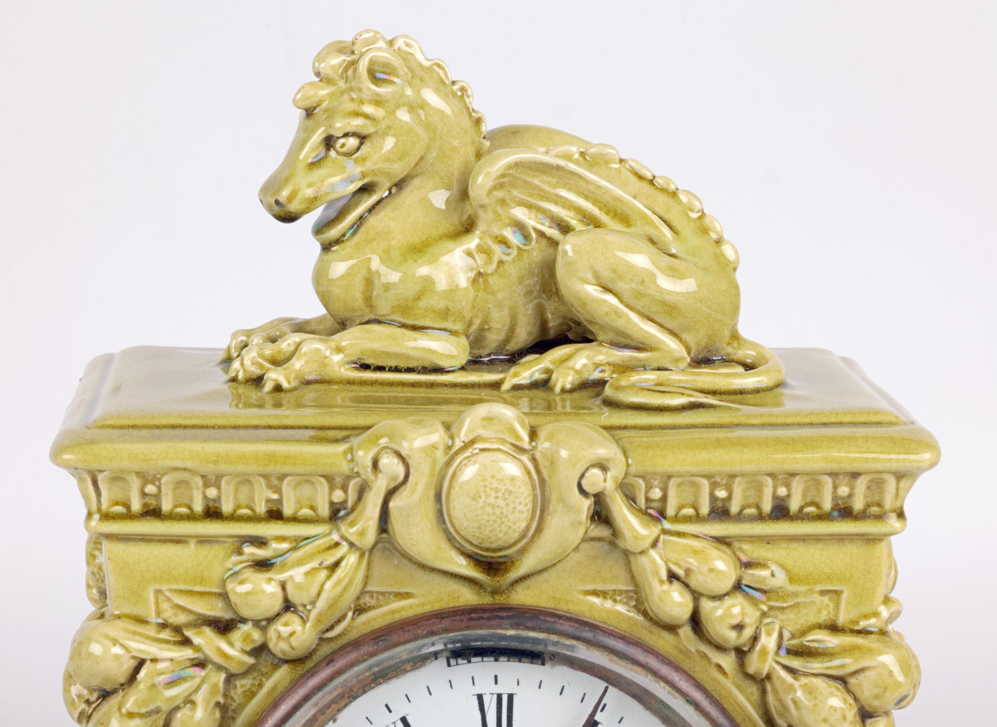 A very rare Burmantofts Faience Arts & Crafts mantel clock of flaring rectangular column shape, cast in relief with fruiting swags and winged putti masks, the top surmounted with a grotesque winged horse like creature dating from around 1890. The