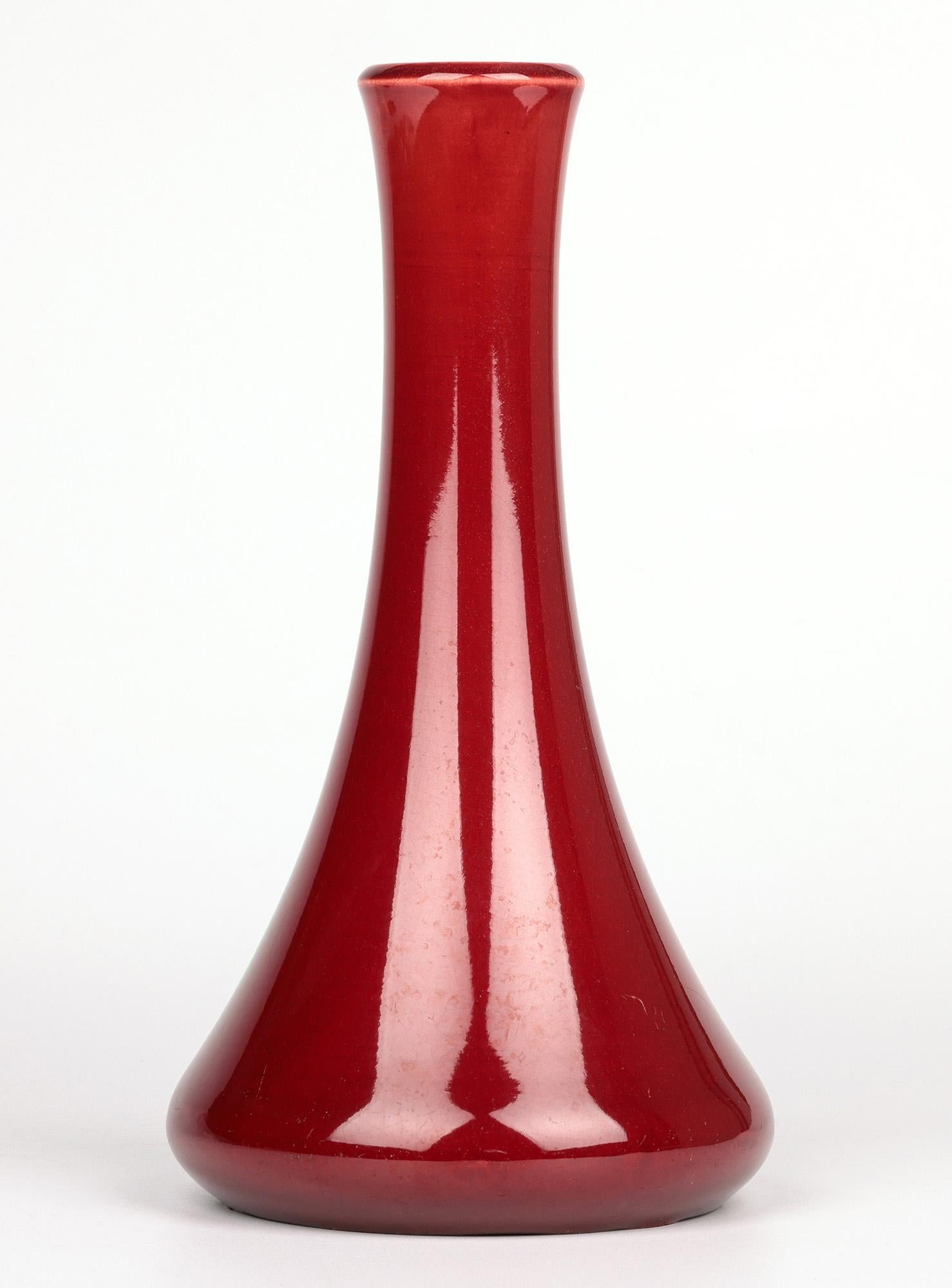 Un elegante vaso in ceramica Burmantofts Pottery decorato con smalti rosso sangue di bue e risalente al 1890 circa. Il vaso di terracotta a forma di fiasco poggia su un ampio piede rotondo con una base ampia e rotonda che si restringe in un collo