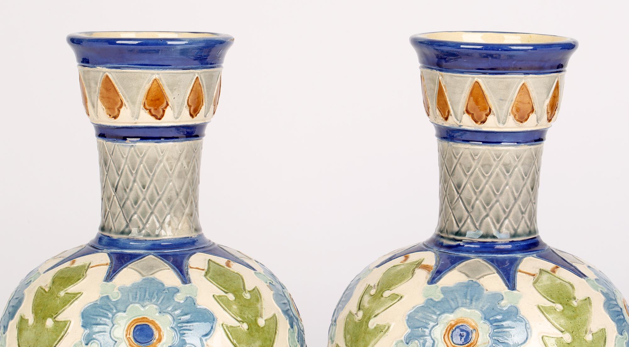A pair Burmantofts Faience Partie-Color bottle vases with floral designs dating from around 1890. The vases have round bodies raised on a narrow round foot rim with flaring cylindrical necks with cup shaped tops and both are modelled in low relief