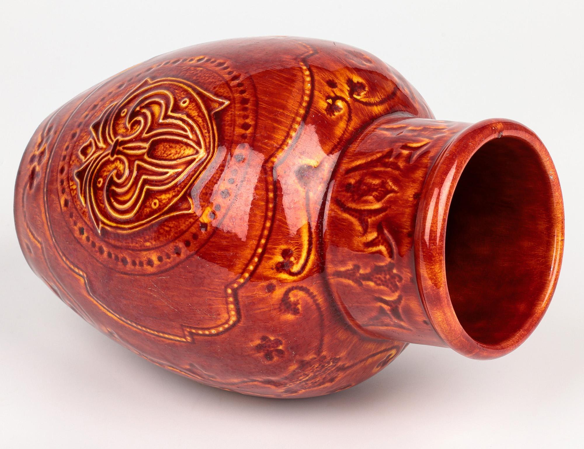 Elegante y poco común jarrón de cerámica artística Burmantofts Faience decorado con un diseño de flor de lis en esmalte rojo sangre de buey sobre fondo amarillo y datado hacia 1890. El jarrón de barro se alza sobre un pie estrecho y redondo sin