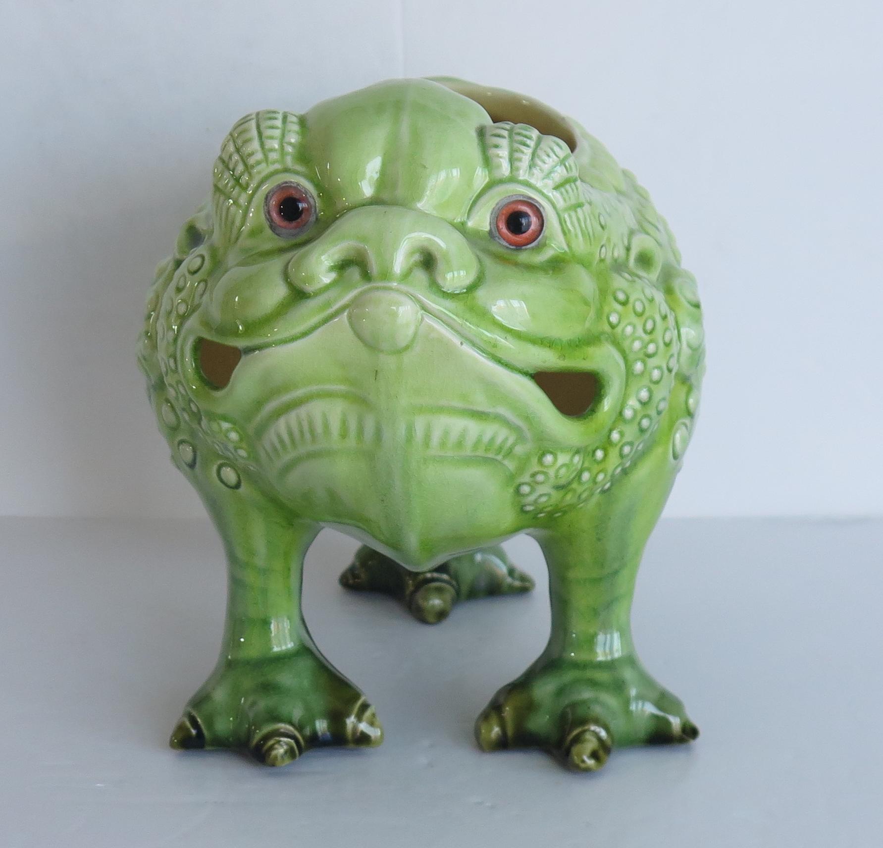 This is a Faience pottery Spoon Warmer modelled as a Bull Frog made by Burmantofts Art Pottery, of Leeds, Yorkshire, England, Circa 1885.

This grotesque animal sculpture is modelled as a scaly three-toed Bull Frog, covered in a green glaze and