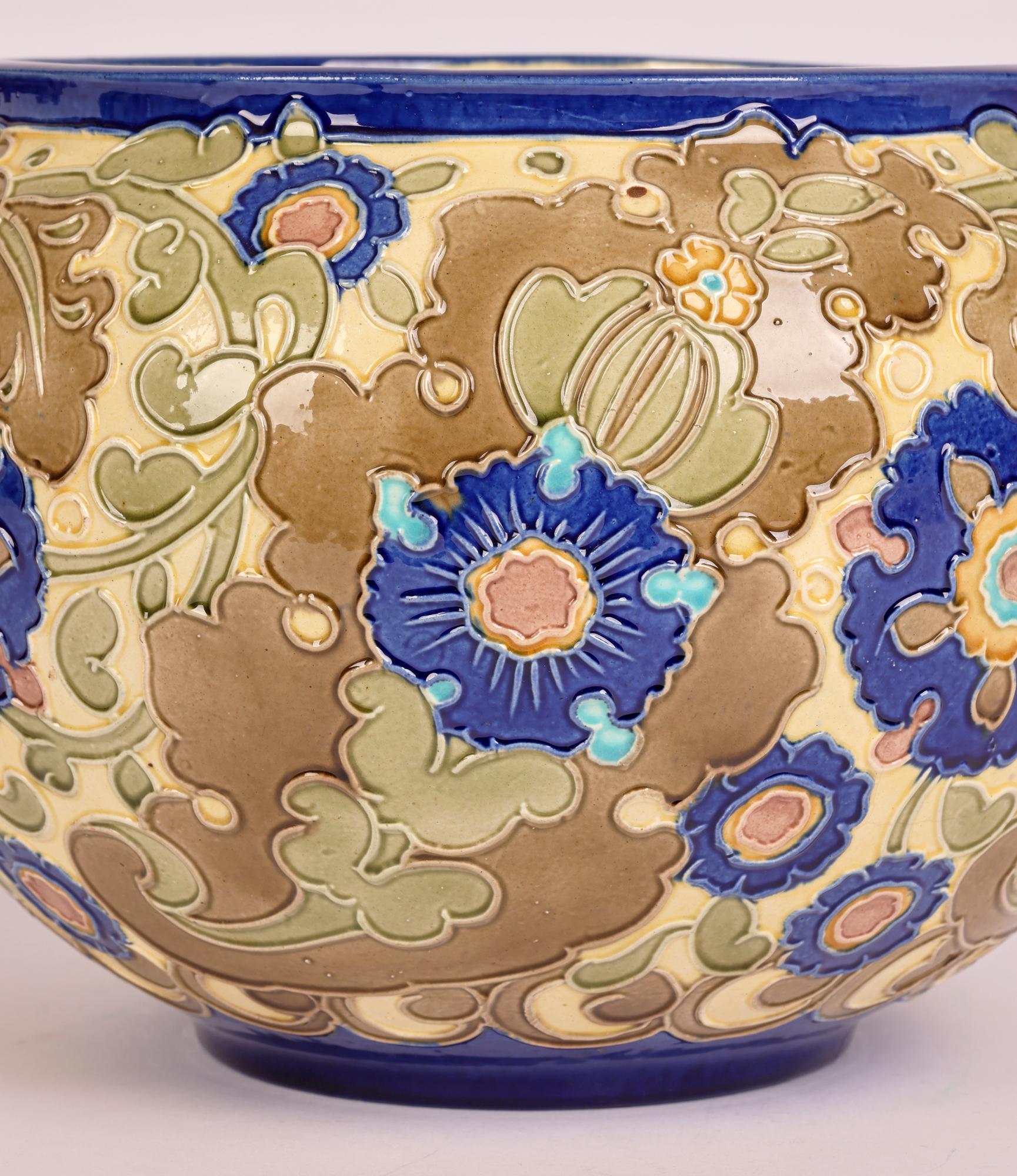A large Burmantofts Faience partie-color pottery planter with scrolling floral designs dating from around 1895. The round earthenware planter stands on narrow round foot with a recessed base and has a wide round shape body narrowing slightly to a