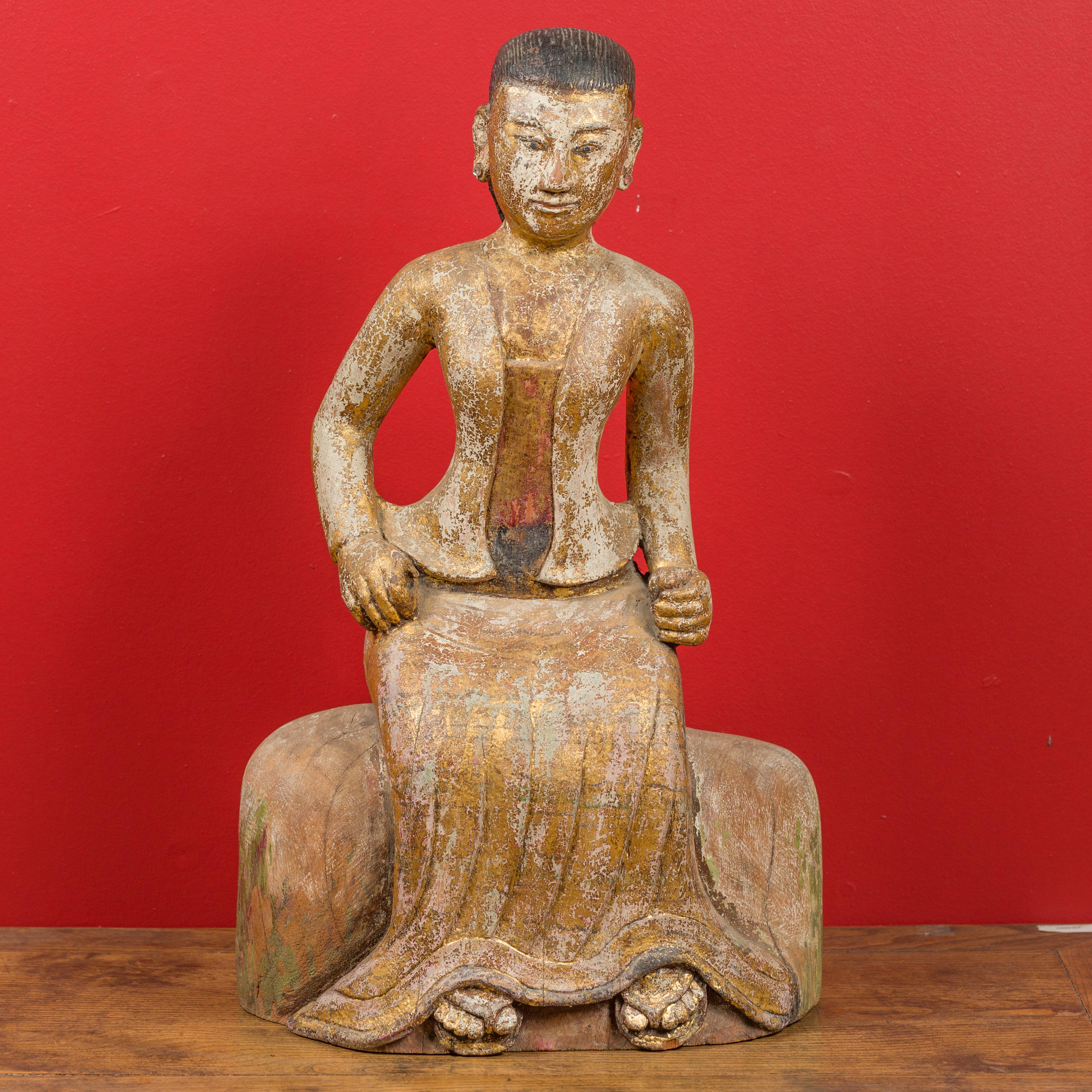 A Burmese hand carved and gilded seated woman statue from the 19th century, in traditional costume. Created in Burma during the 19th century, this sculpture depicts a woman wearing a gilded traditional Burmese costume with sandals, and showcases