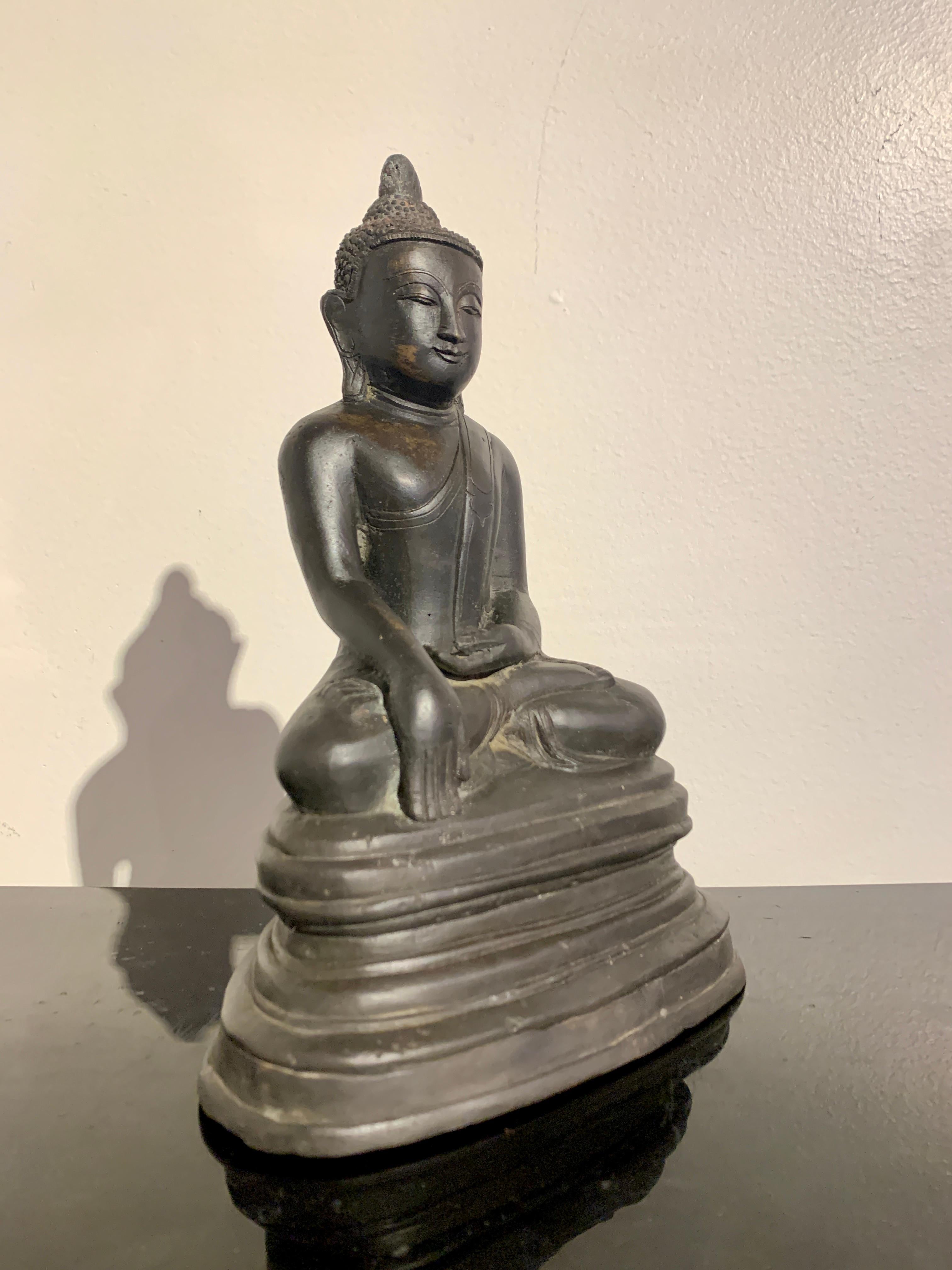 A delightful Burmese cast bronze Buddha in the Arakan style, mid 20th century, Myanmar (Burma).

The Buddha sits in the full lotus position, the soles of his feet turned up. His hands perform bhumisparsha mudra, the gesture of calling the earth to