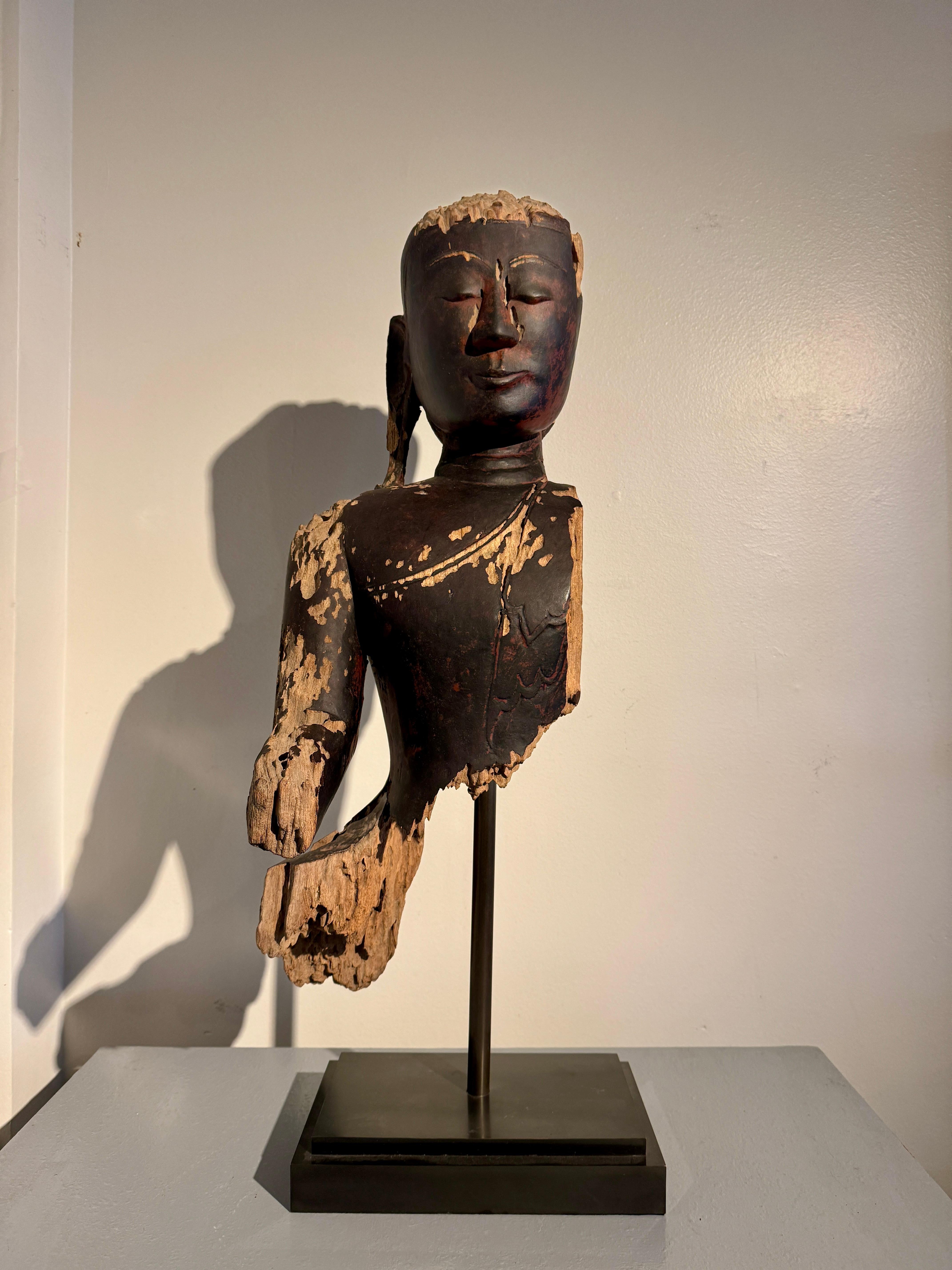 A mysterious and evocative heavily weathered and fragmentary bust of a Burmese standing Buddha, Ava Period, late 17th or early 18th century, Burma (Myanmar). 

The near life-sized image of the Buddha is carved from a single timber, and would