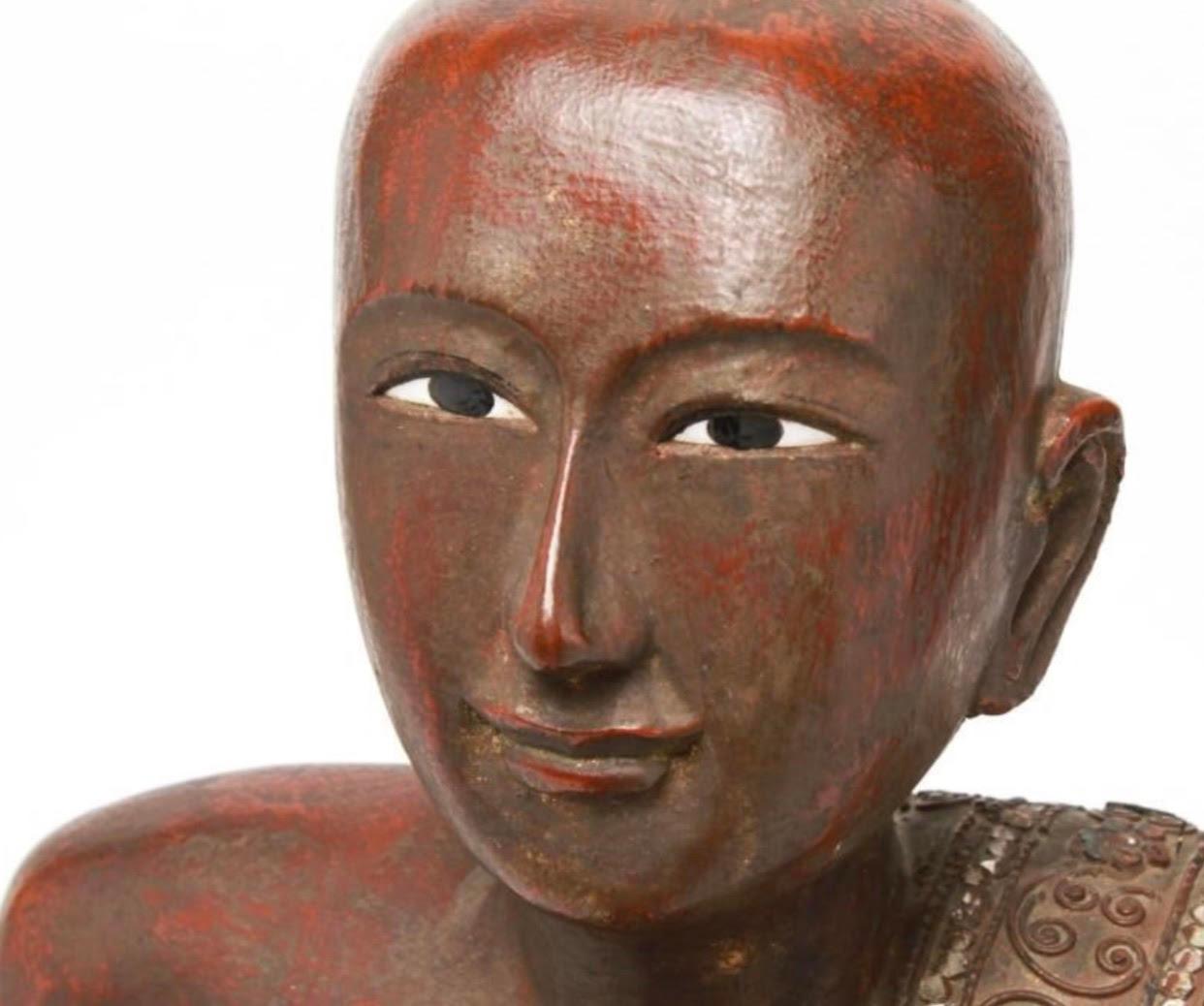 Burmese hand carved wood statue of a Buddhist monk, with traces of gilt and red lacquer. Made in the 20th century. The figure has enameled eyes fixed in an intense yet spiritual upward enigmatic gaze. The monk’s attire is detailed with glass