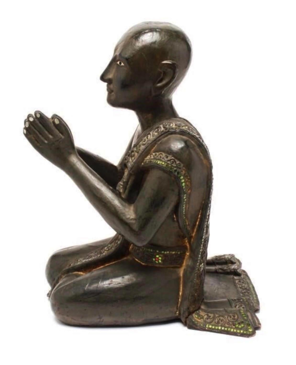 Burmese hand-carved hardwood statue from the 20th century depicting a Burmese Monk praying in adoration of Buddha. The Monk’s garment contains a sprinkling of mirrored “jewels” and the enameled eyes focus upward in an intense gaze. In great antique