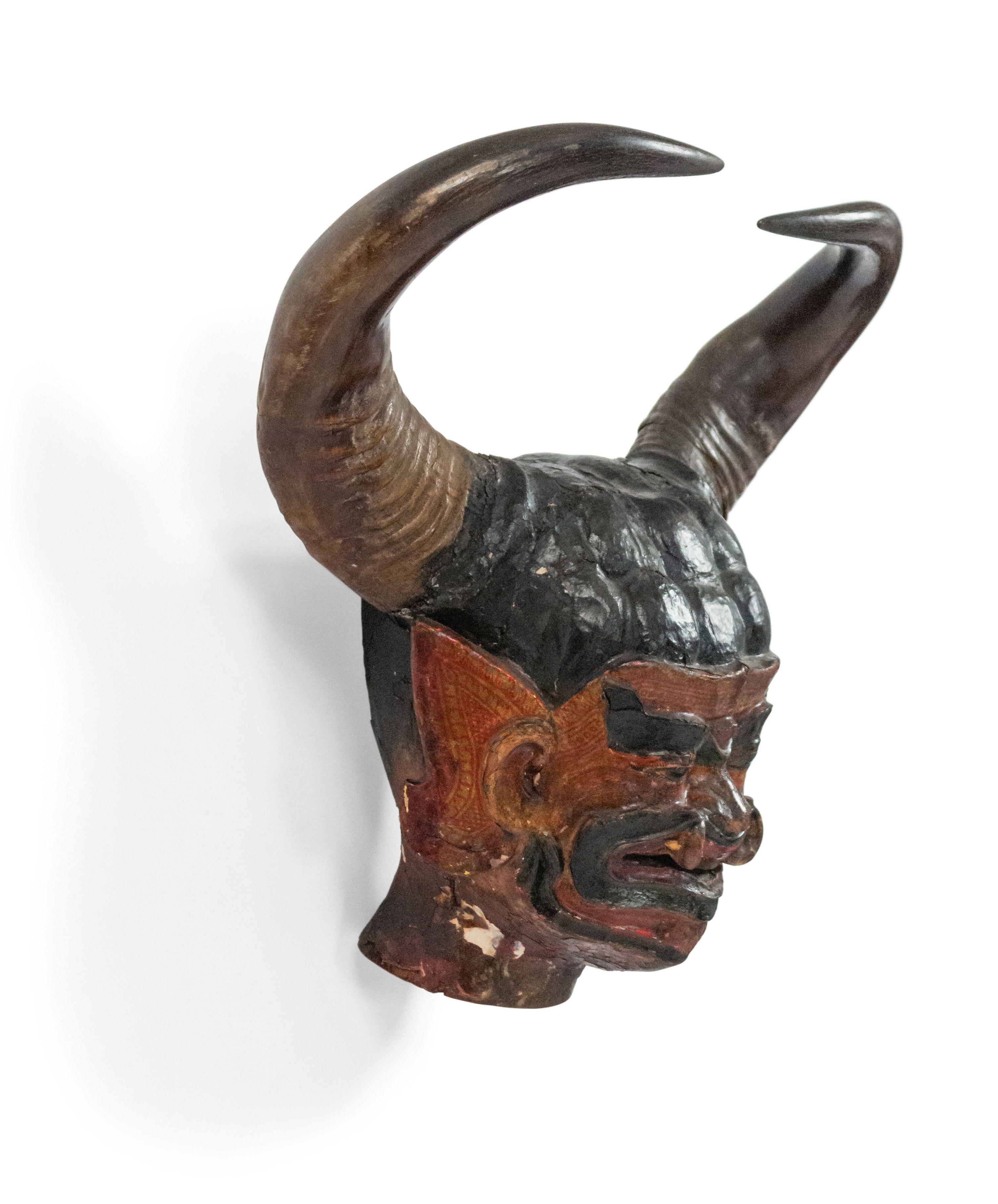 Asian Burmese style (19th Century) carved and painted wall plaque of head of grotesque figure with taxidermy horns.
 
