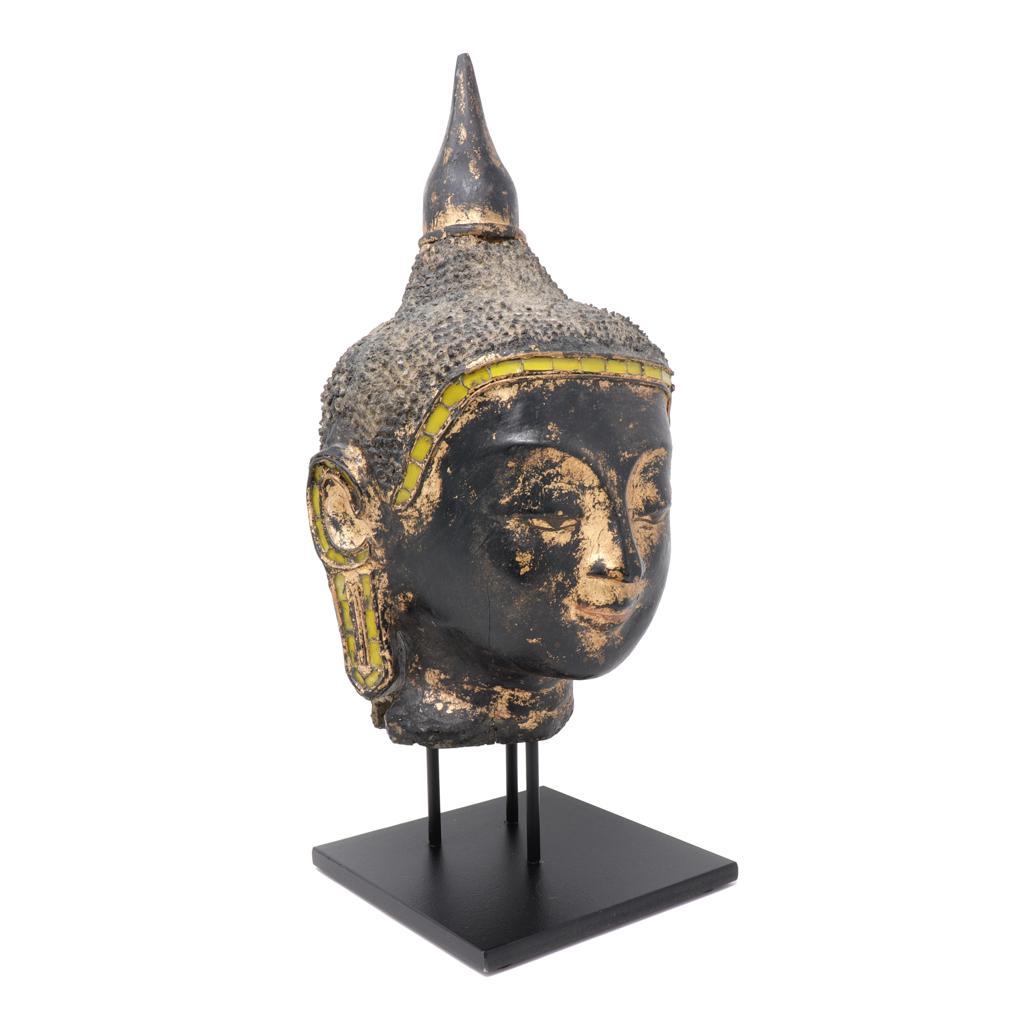 Burmese Dry Lacquer Head from a seated Buddha image, Shan States. The black lacquer head with enigmatic smiling expression, downcast eyes, over arching eyebrows, yellow glass inset hairline, long earlobes and small durian spine type hair with a