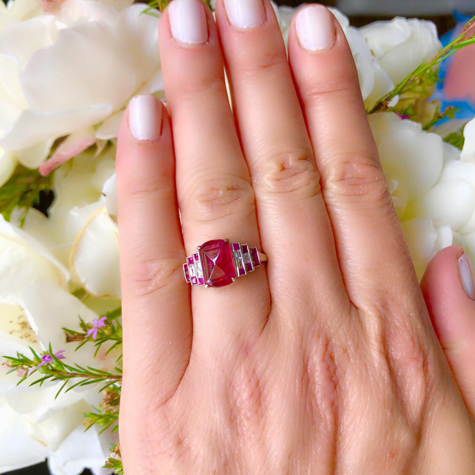 18k white gold Deco style ring featuring a 2.88 carat Burmese fancy reddish pink sapphire with steps of calibre cut rubies and baguette diamonds highlighting the main stone. The ring measures 10.5mm to 1.5mm wide and is currently a size 7.0 with