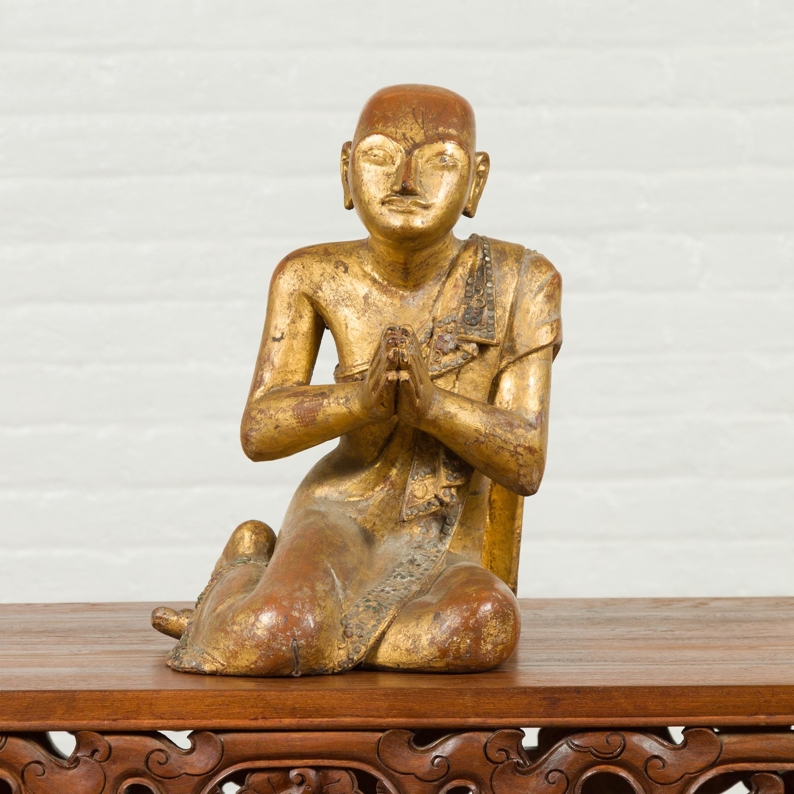 A Burmese hand carved giltwood statue of a seated Buddhist monk with mica inlay and distressed patina from the mid-20th century. Born in Burma during the midcentury period, this hand carved giltwood statue features a seated Buddhist monk, his hands