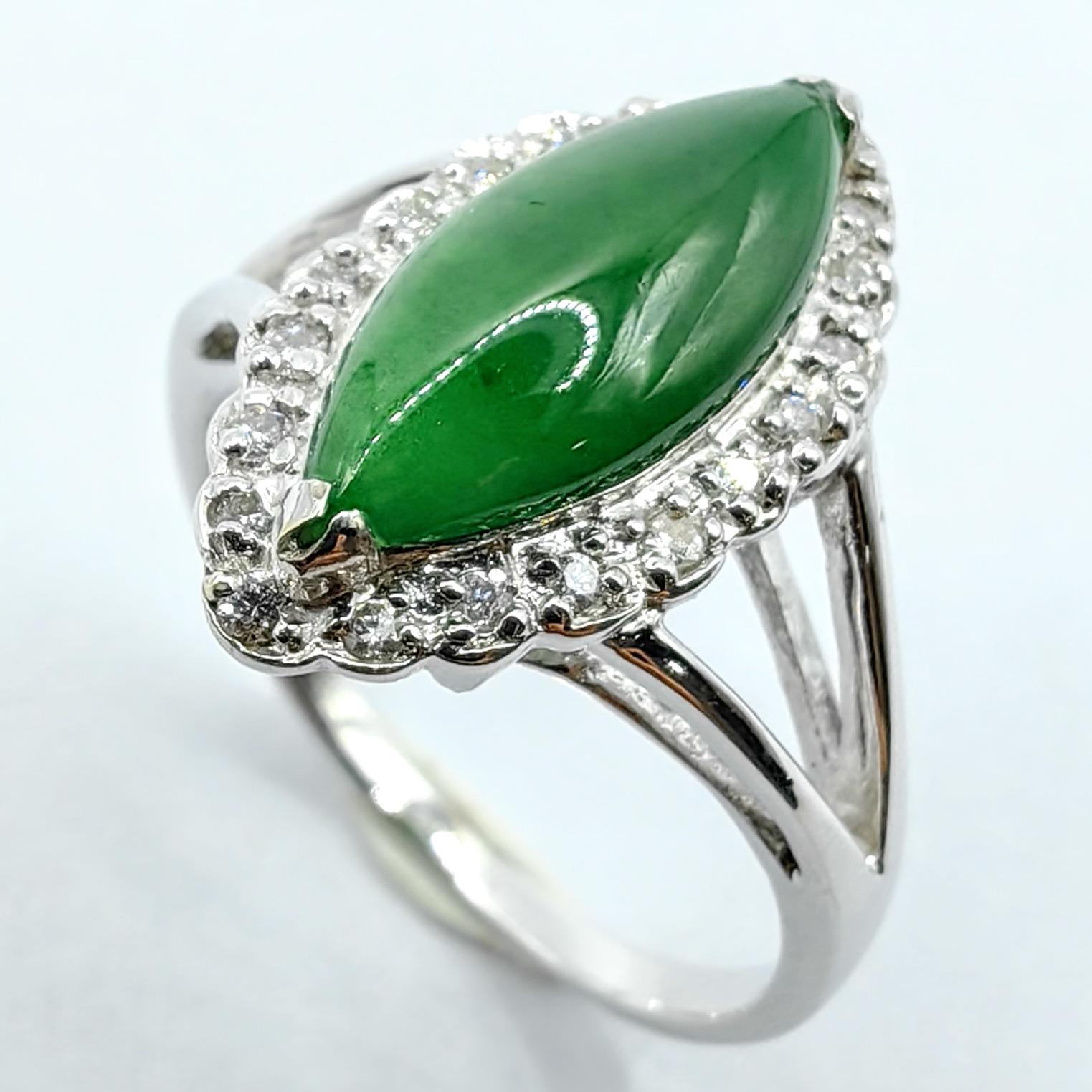 Dieser elegante Ring zeichnet sich durch einen markanten marquiseförmigen Cabochon aus echtem burmesischem Jadeit in einem leuchtenden Grünton aus, der von einem Kranz aus zwanzig runden Diamanten im Brillantschliff eingerahmt wird, die in 18 Karat