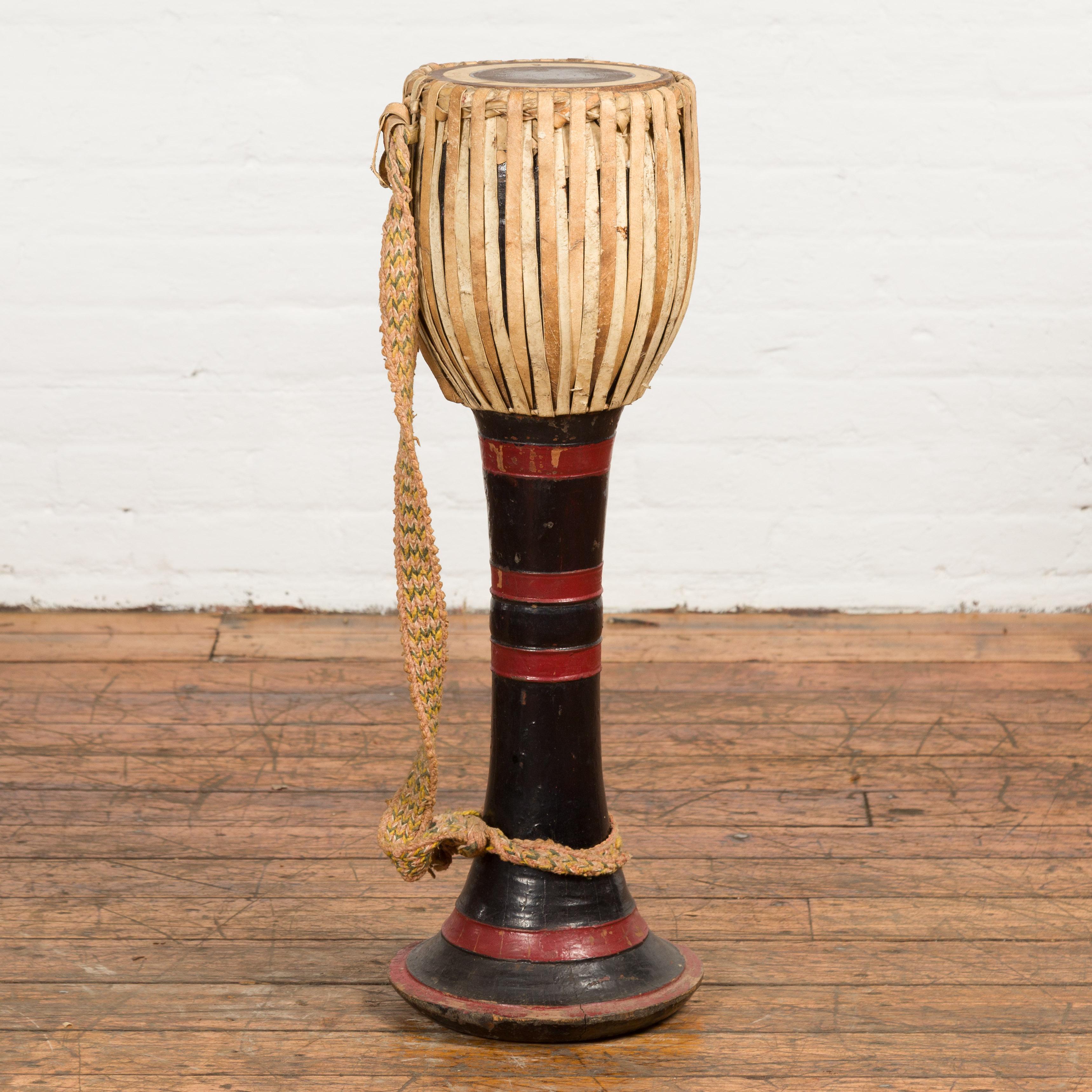 A Burmese tribal Ozi goblet shaped teak drum from the late 19th century, with red and black lacquer and calf skin top. Created in Burma during the later years of the 19th century, this tribal drum, called an Ozi drum, features a goblet shaped top
