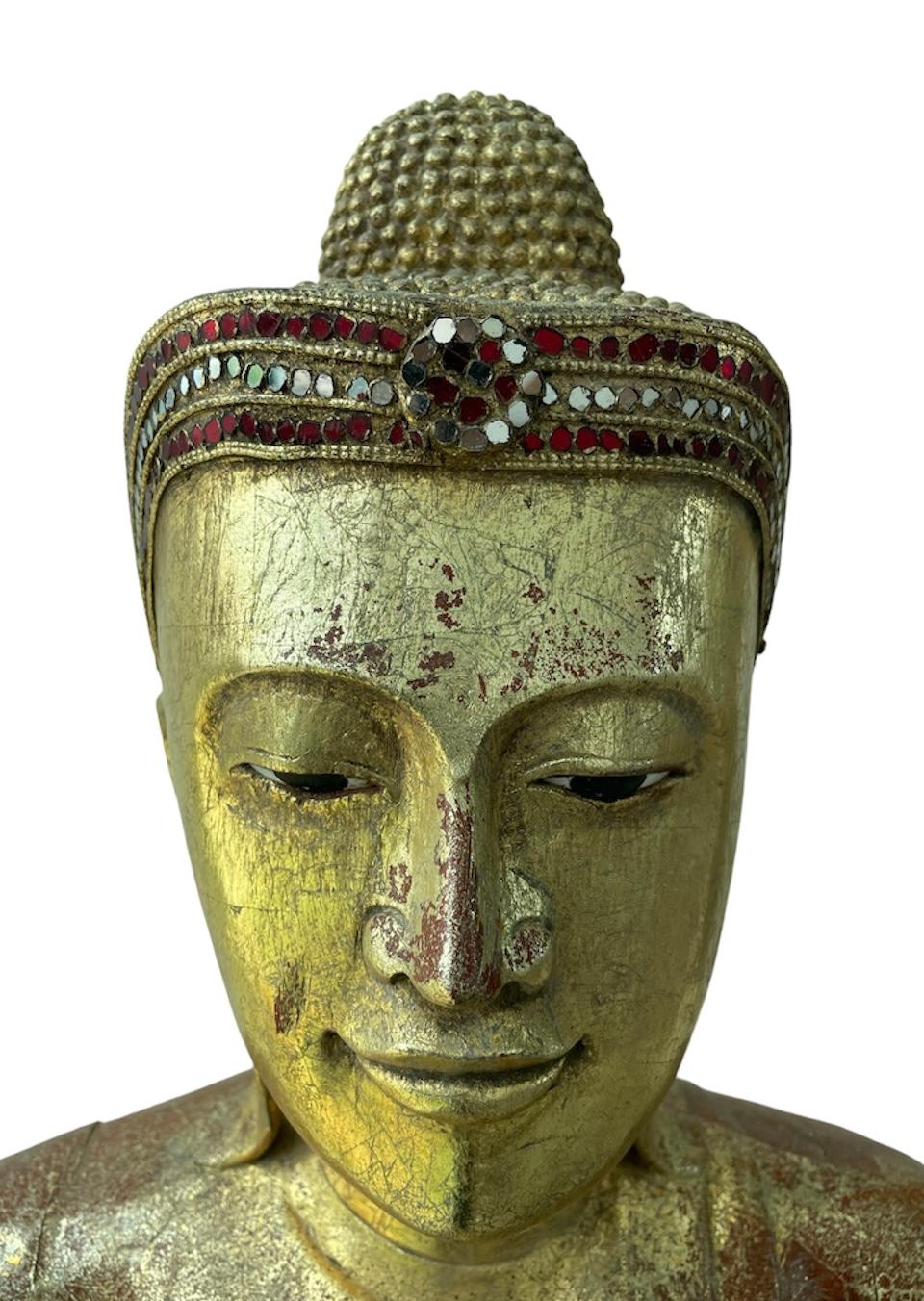 Questa è una scultura di Buddha birmana. Raffigura un Buddha di Mandalay in legno dorato in piedi su un fiore di loto con occhi molto espressivi. La sua testa è ornata da una corona fatta di pezzi di vetro rotondi. La scultura del Buddha è sostenuta