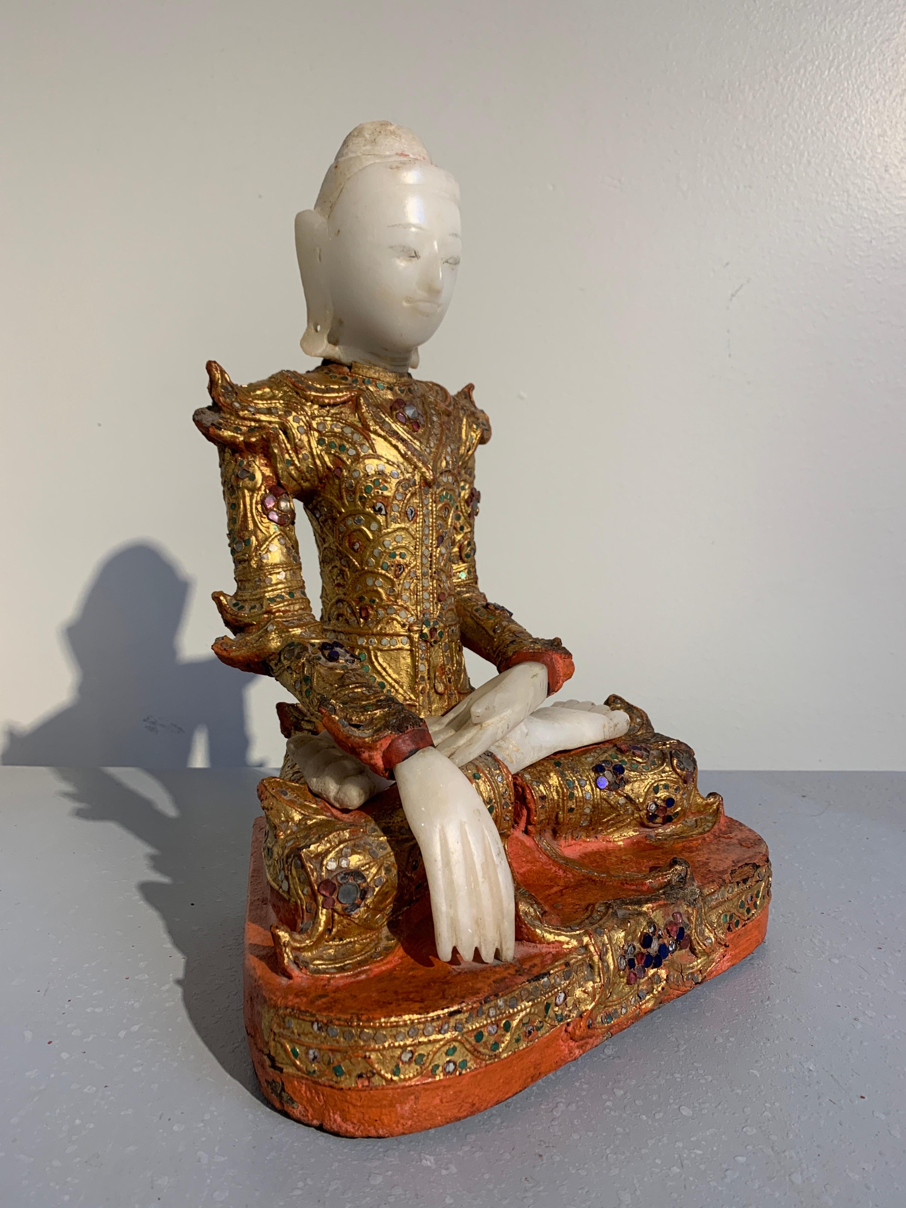 A resplendent Burmese Buddha in royal attire, known as Jambupati, carved from teak, lacquered, gilt and embellished with glass 