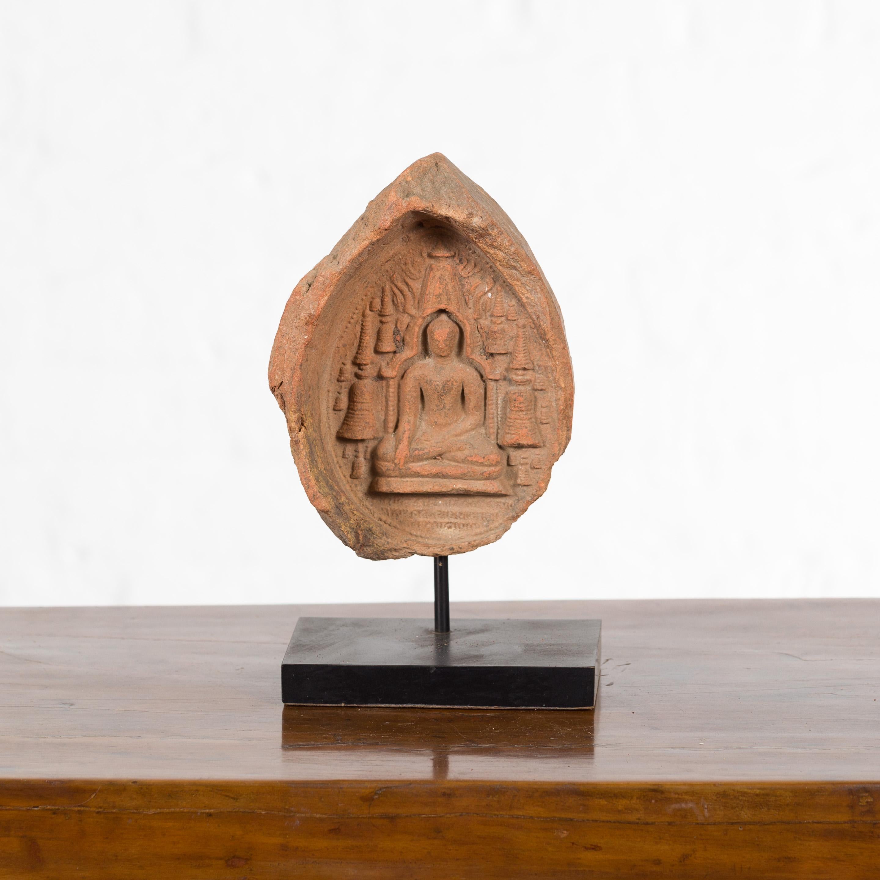 A Burmese Pagan Empire terracotta votive Buddha sculpture from the 12th or 13th century, mounted on a custom stand. Created in Burma during the Pagan Kingdom, this votive terracotta bas-relief depicts the Buddha calling the Earth to Witness, holding