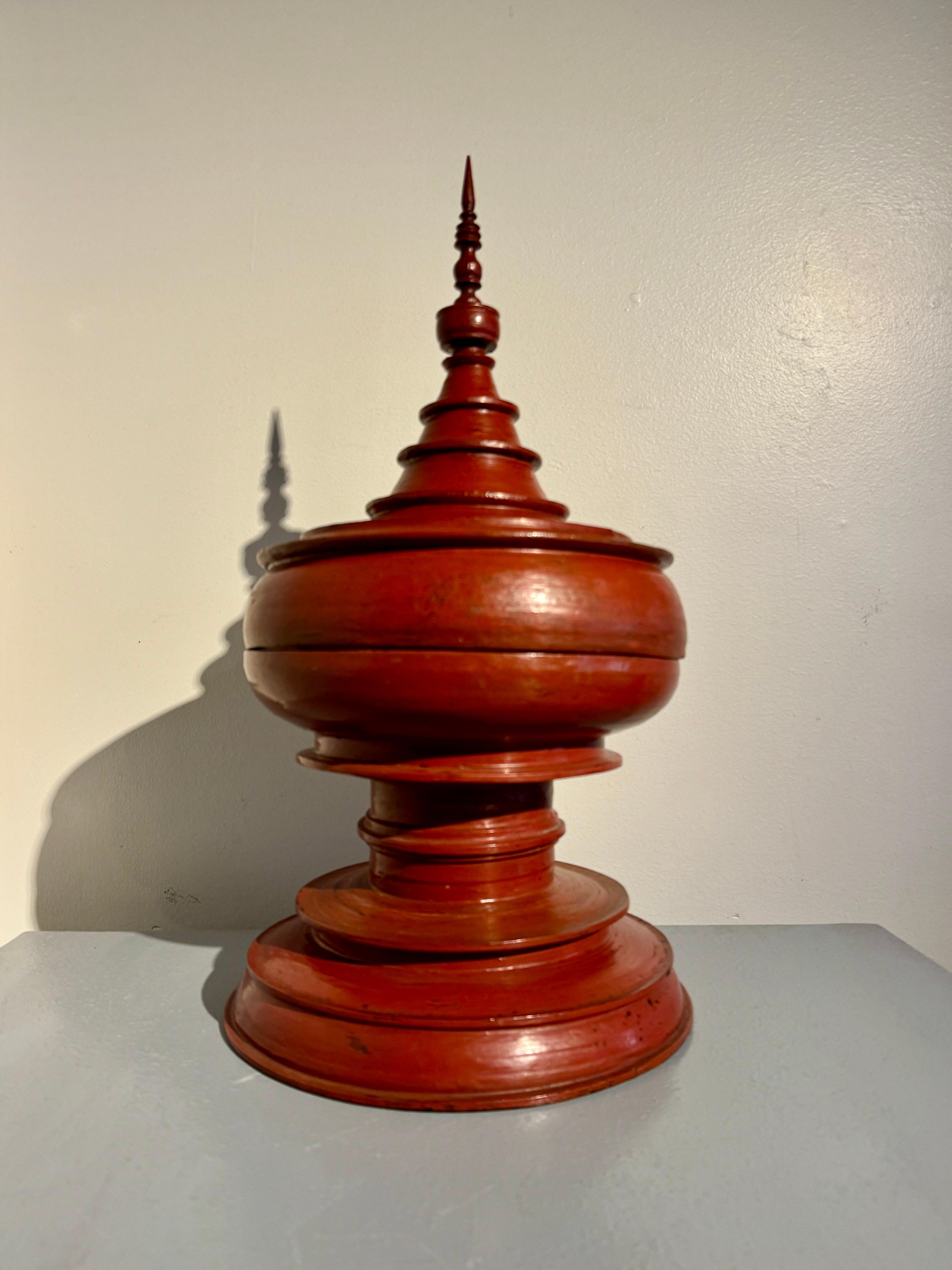 A striking Burmese red lacquered stupa-shaped offering vessel, hsun-ok, early 20th century, circa 1920, Burma (Myanmar). 

The hsun-ok of traditional stupa form, featuring a stepped pedestal base supporting a wide bowl with an interior tray, and a