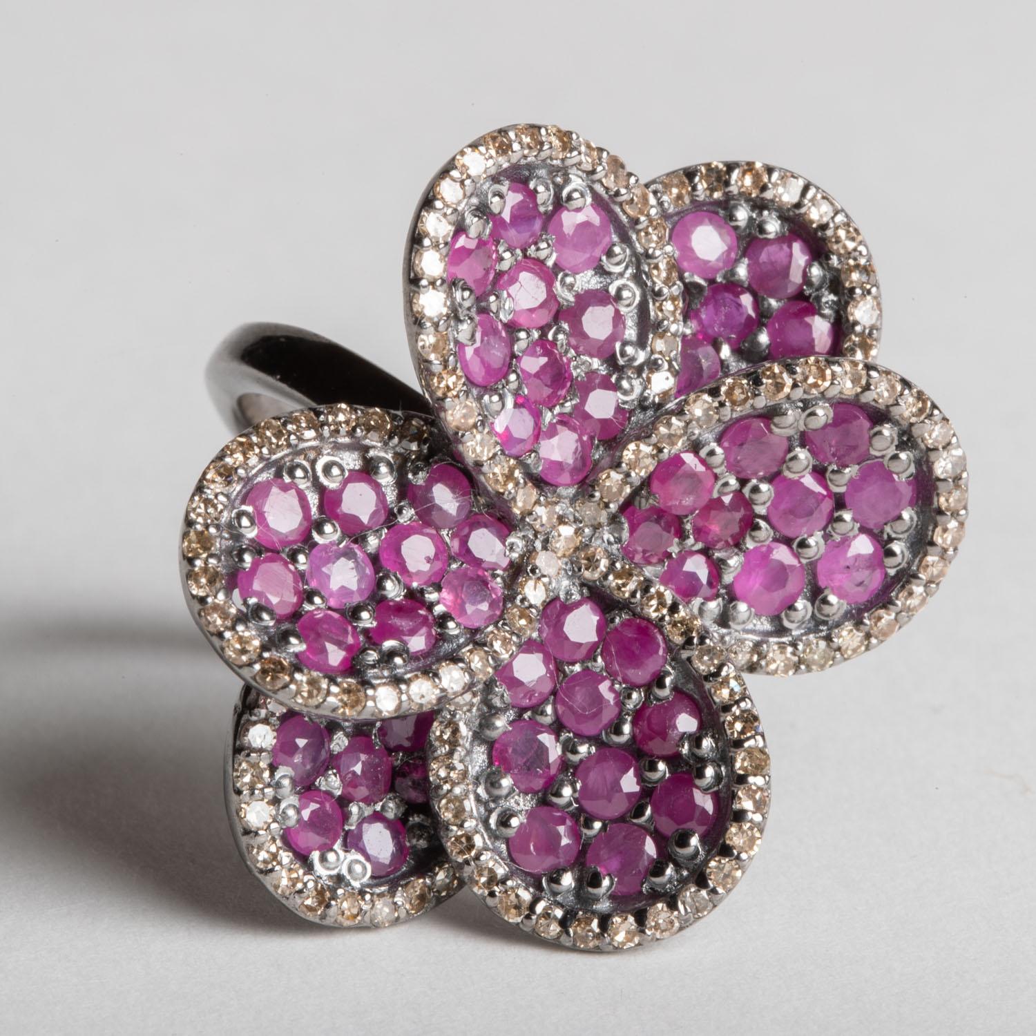 A striking ring of flower petals in round, faceted Burmese pink rubies bordered with round, brilliant cut diamonds, all in a pave` setting.  In sterling silver.  Ring size is 7.75.  Carat weight of rubies totals 5.22; diamonds total 1.12 carats. 