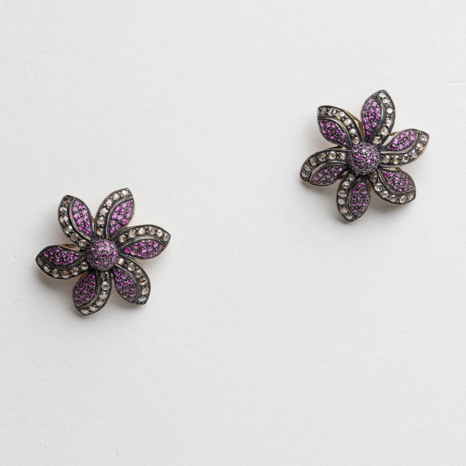 A dramatic pair of floral-motif stud earrings featuring pave`-set round, brilliant cut Burmese pink rubies and diamonds.  18K gold backs for pierced ears.  Rhodium plated over sterling silver.