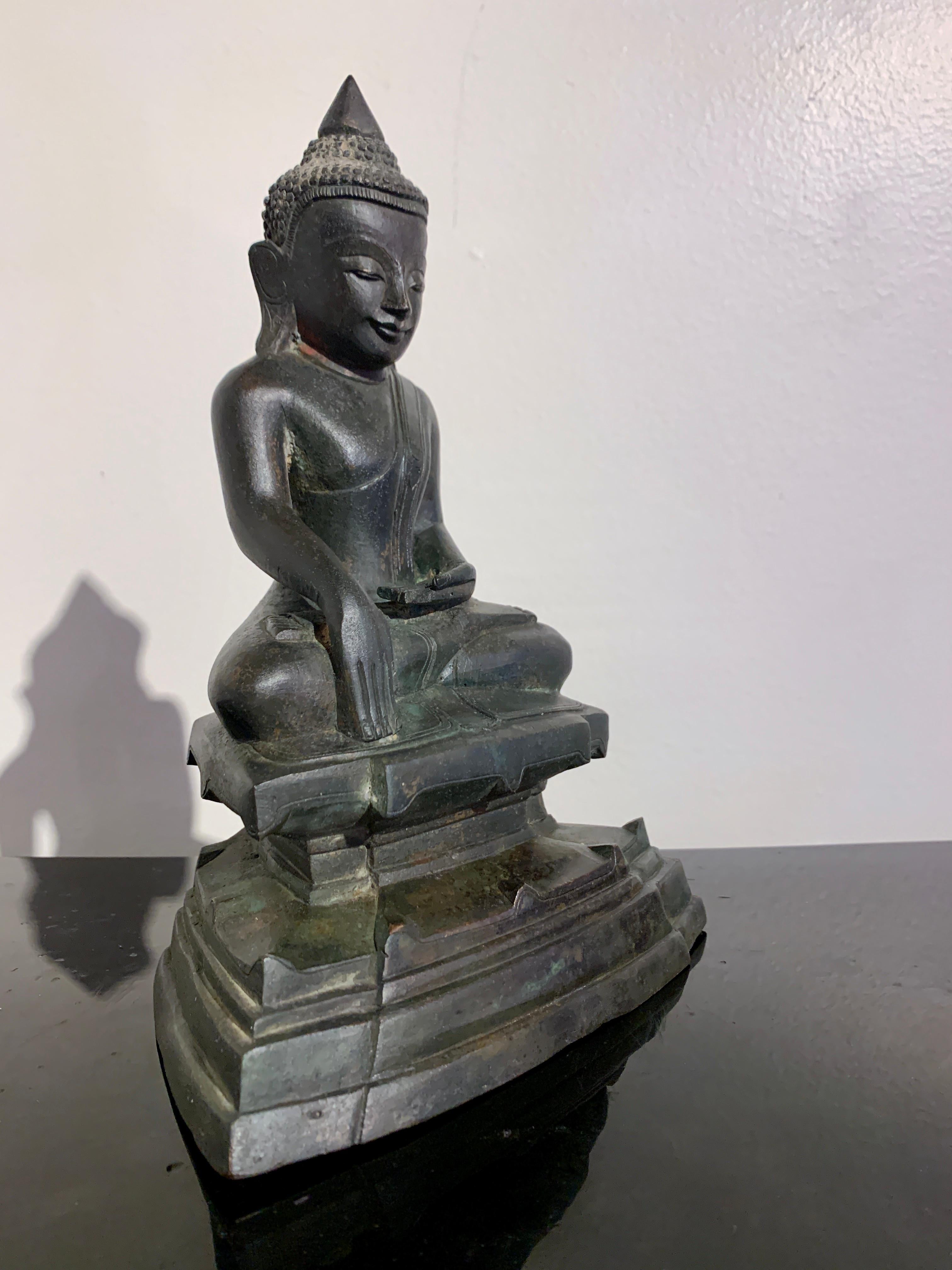 A nice and classic Burmese Shan cast bronze Buddha in the Ava style, 19th century or earlier, Burma. 

The Buddha sits upon a stepped and waisted stylized double lotus pedestal, legs in the full lotus position, his hands performing bhumisparsha