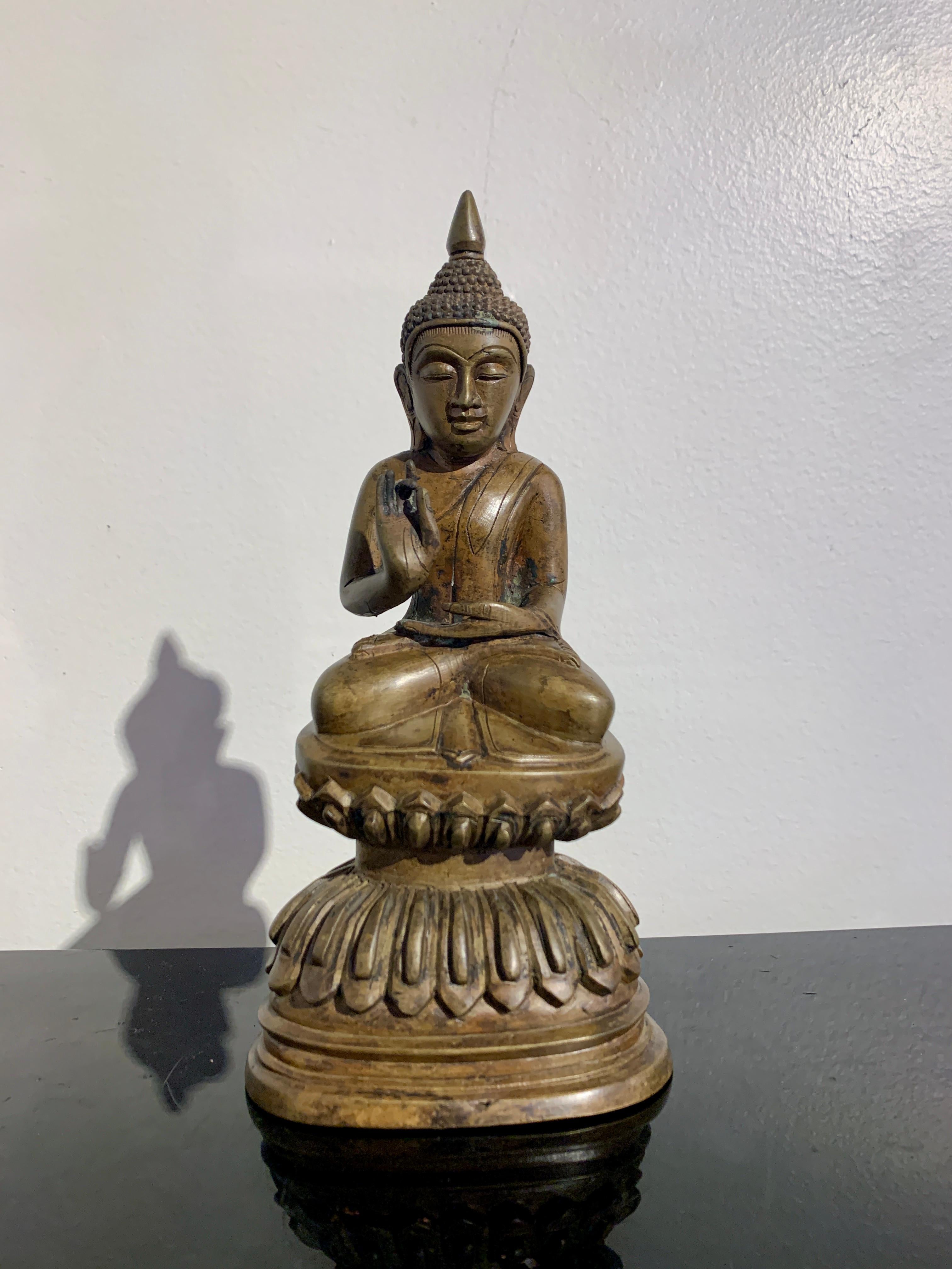 A delightful Shan Burmese cast bronze seated Buddha in the Ava style, late 19th or early 20th century, Burma.

The Buddha sits upon a high, well cast double lotus pedestal. He is seated pitched forward in the full lotus position, the soles of his